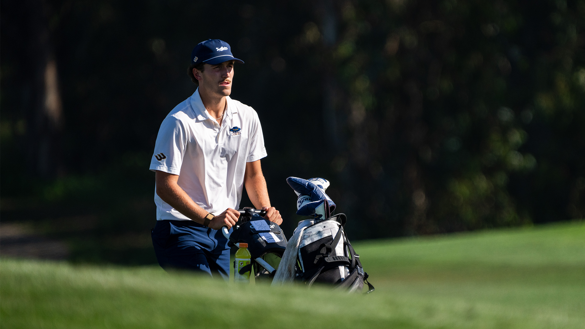 Jack Watters pushes his cart up the hill as he walks towards his ball to hit his next shot.