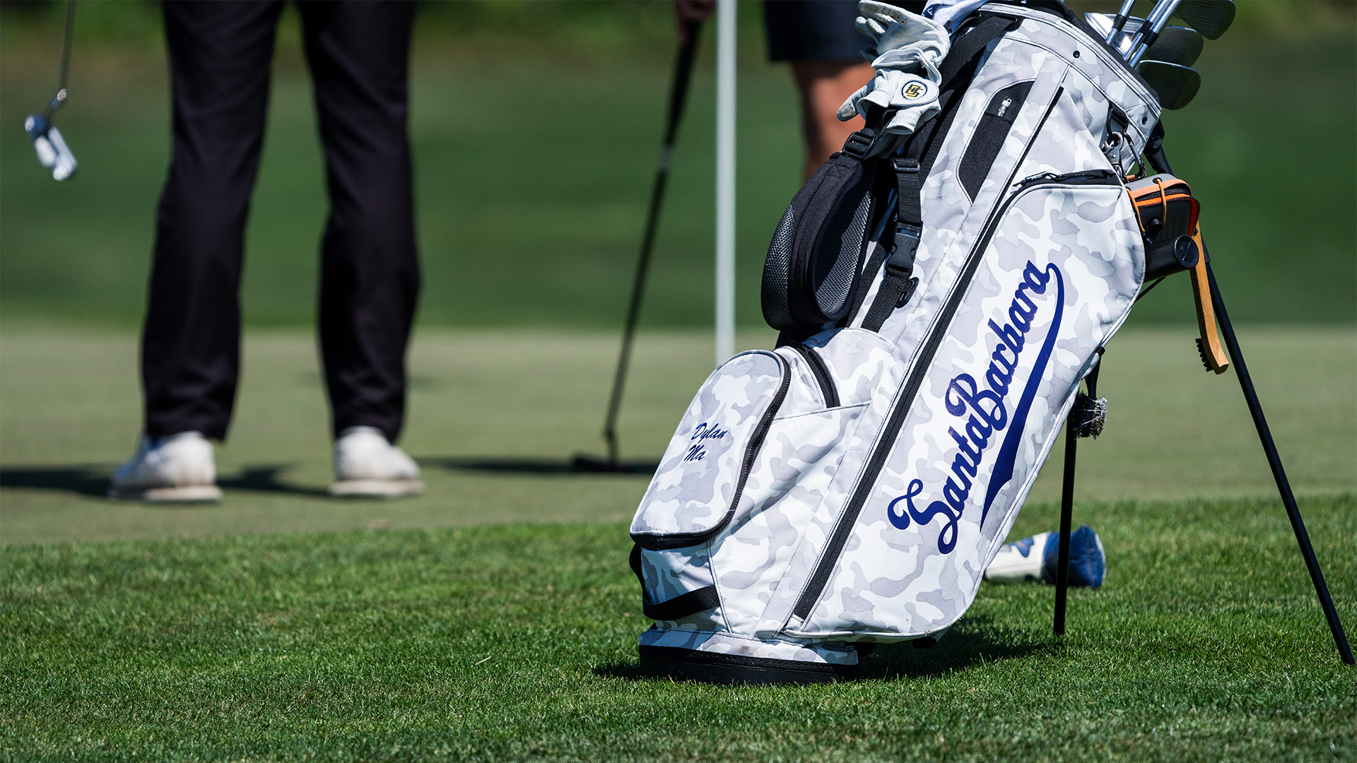 A golf bag with Dylan Ma's name in script standing up on grass.