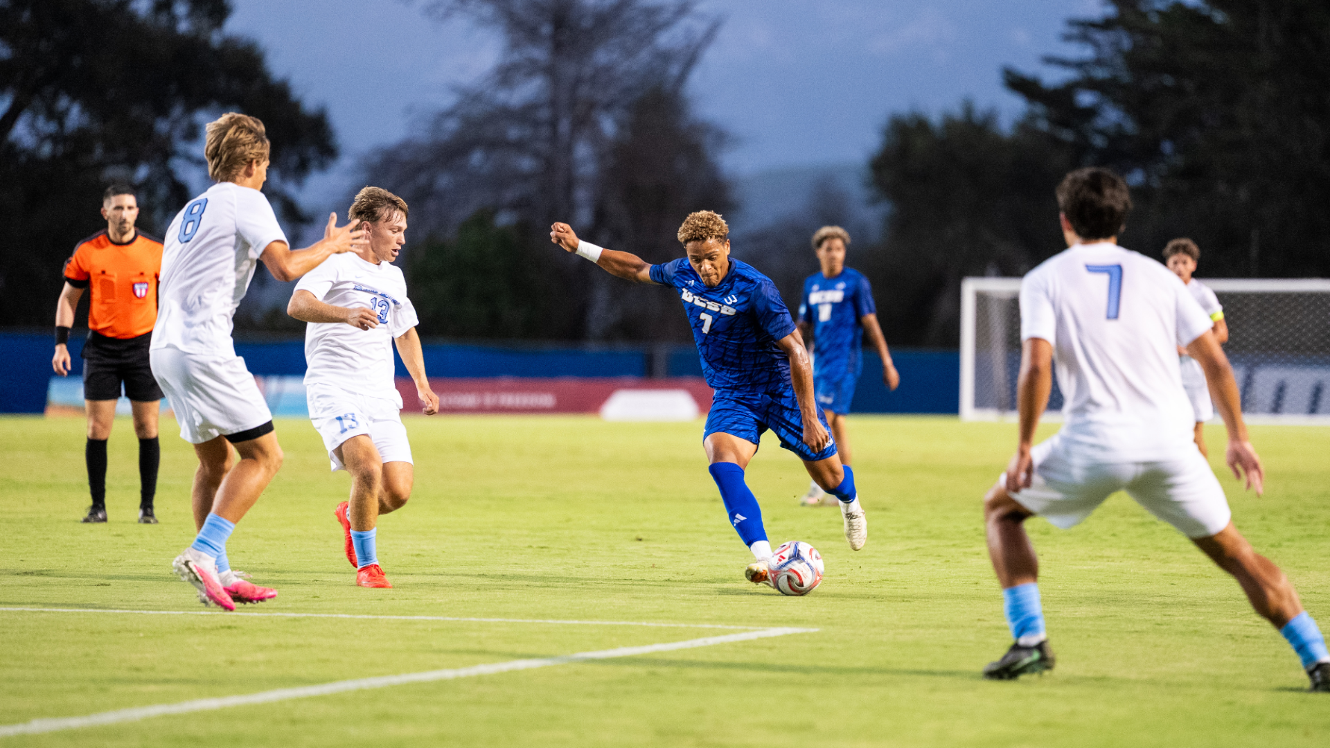 #7 Donovan Sessoms winds up to take a shot, with defenders in white to his left, right and front, but all about a yard away