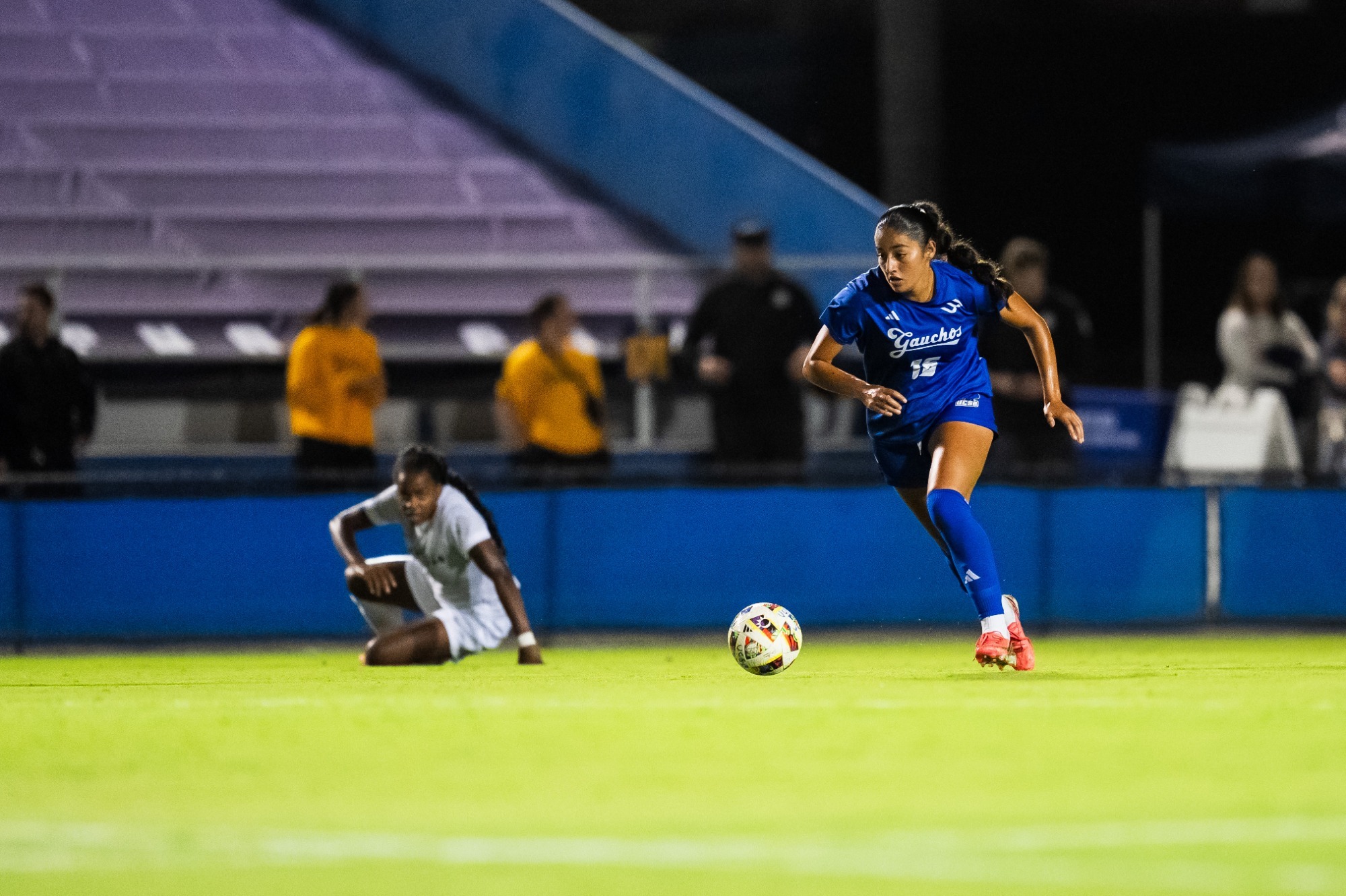 Delilah Vega-Aguilar hustles after a ball in the middle of the field with a Long Beach State defender down behind her.