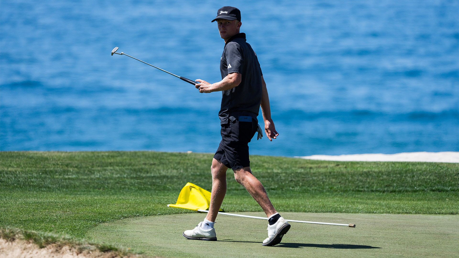Ryan Gay walking away after completing a hole at Sandpiper Golf Course with his putter in hand and the flag laying on the ground behind him.