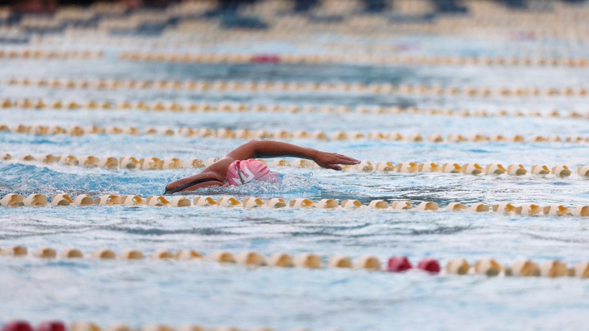 UC San Diego swimmer in pink cap swims freestyle stroke during a race