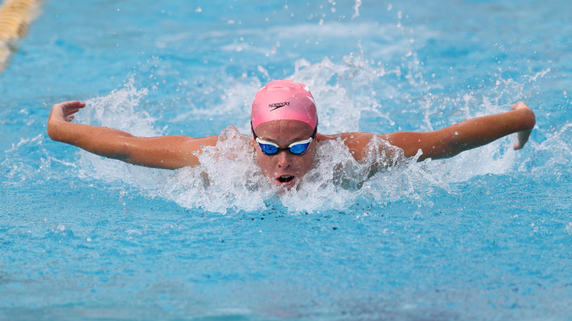 Addison Everage swimming butterfly, wearing a pink swim cap and goggles