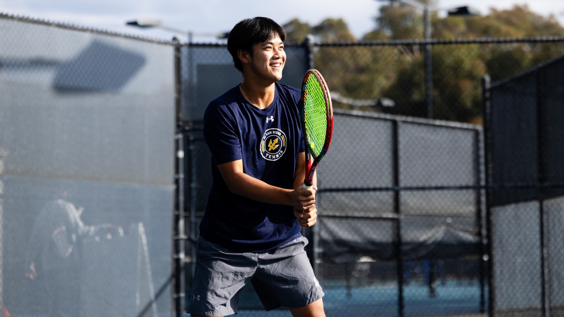 Trevor Nguyen smiles holding a tennis racquet