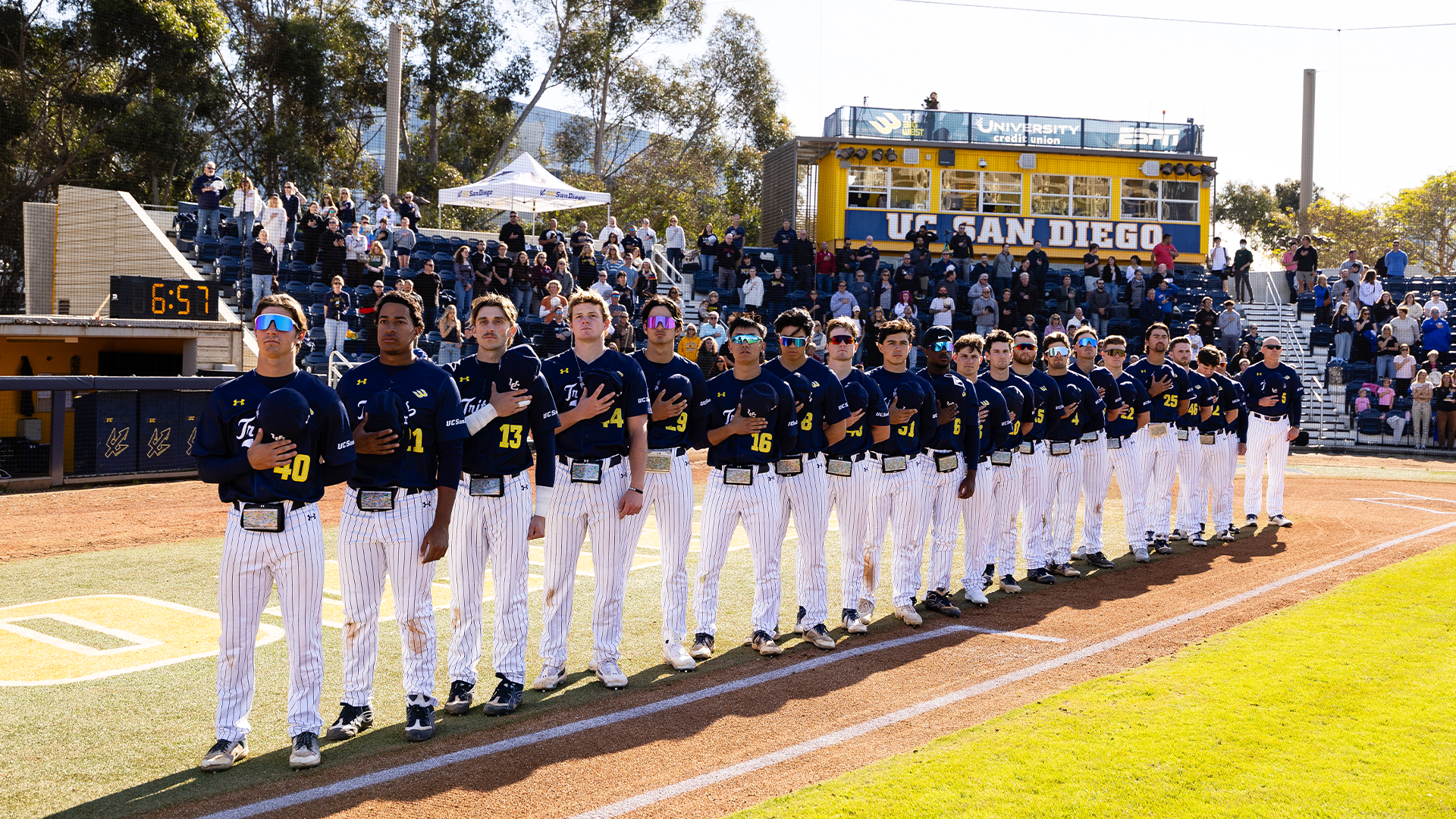 Baseball team stands with caps removed for national anthem with stadium seats in background