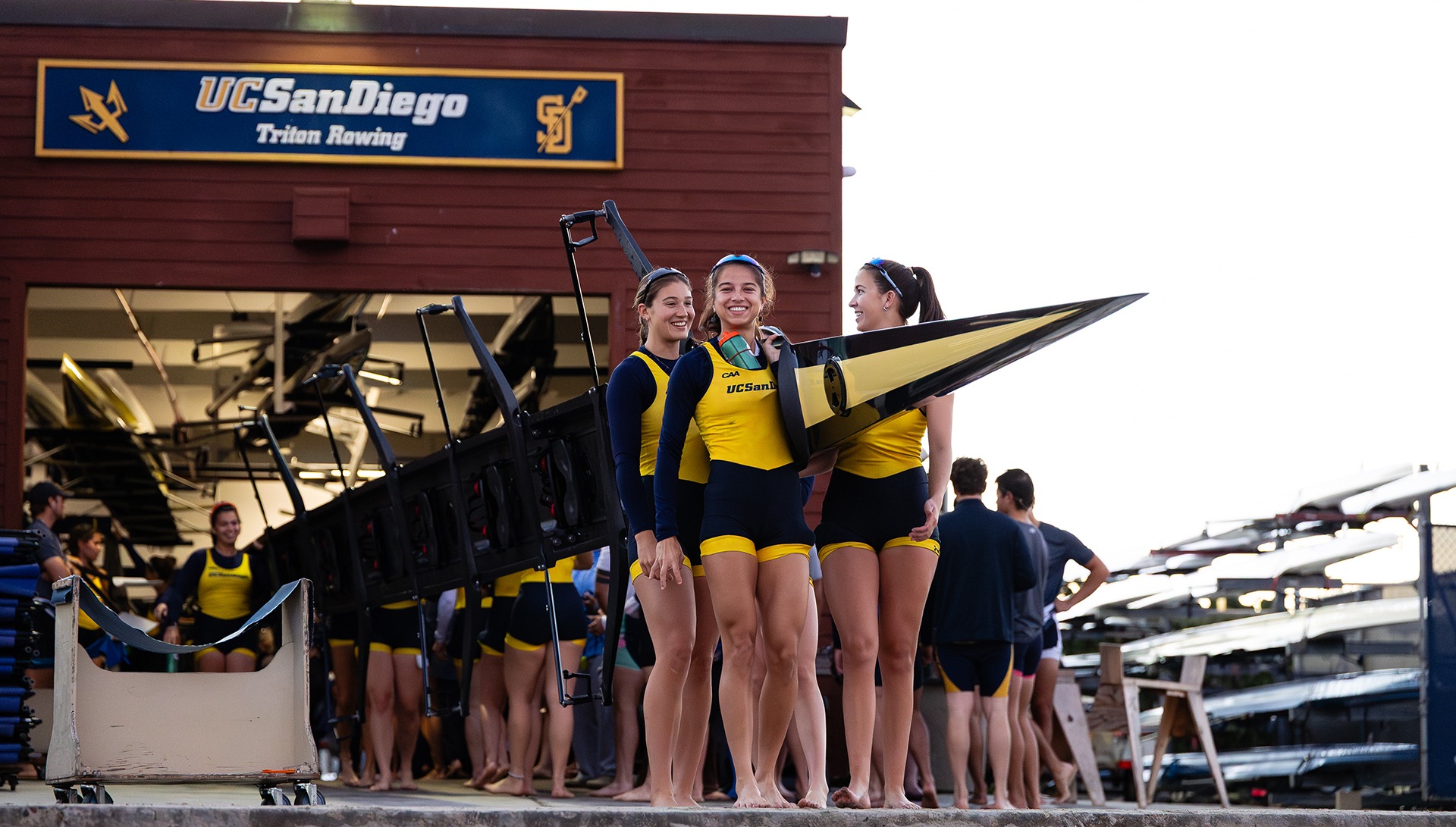 Members of the UC San Diego women's rowing team carry a boat from the boathouse to the water.