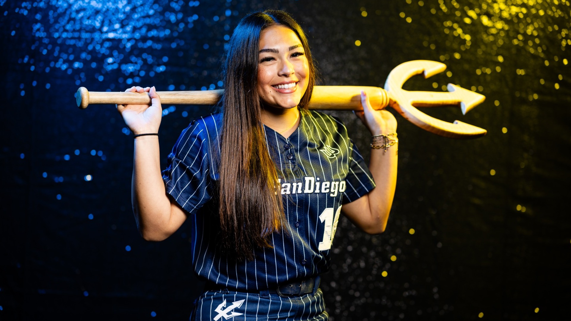 Tori Hinostro poses with a trident behind her head in a blue uniform with white pinstripes at UC San Diego softball media day