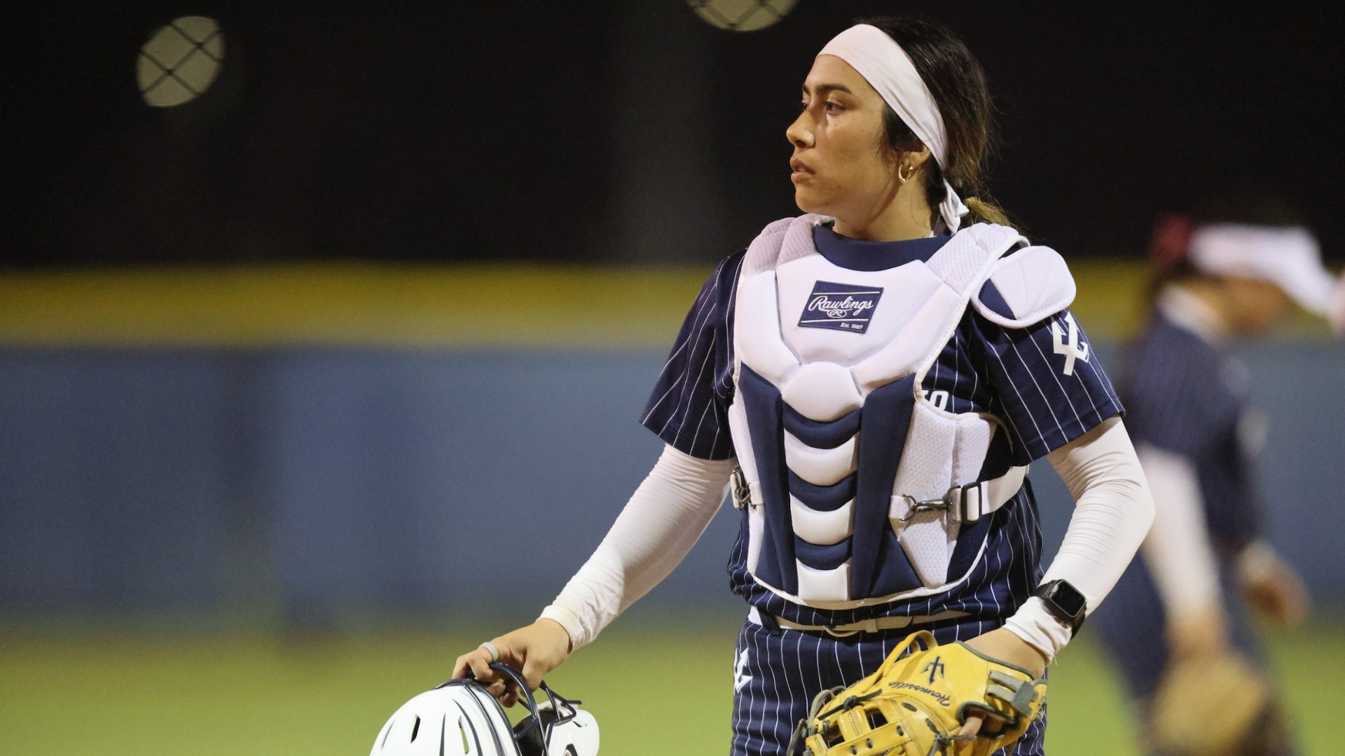 Catcher Lily Hermosillo from UC San Diego softball holds her catcher's mask in her right hand with her glove on her left