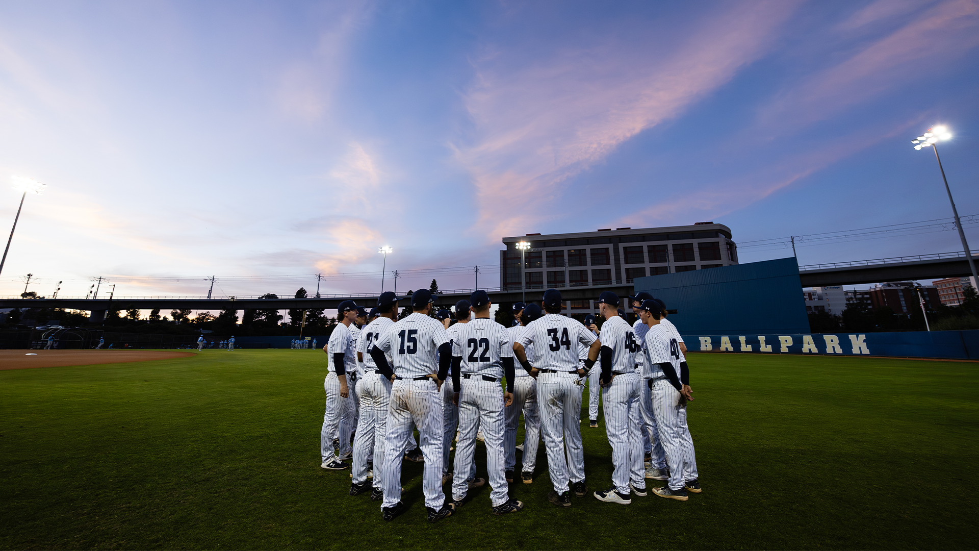Team huddle with sunset and ballpark outfield in background
