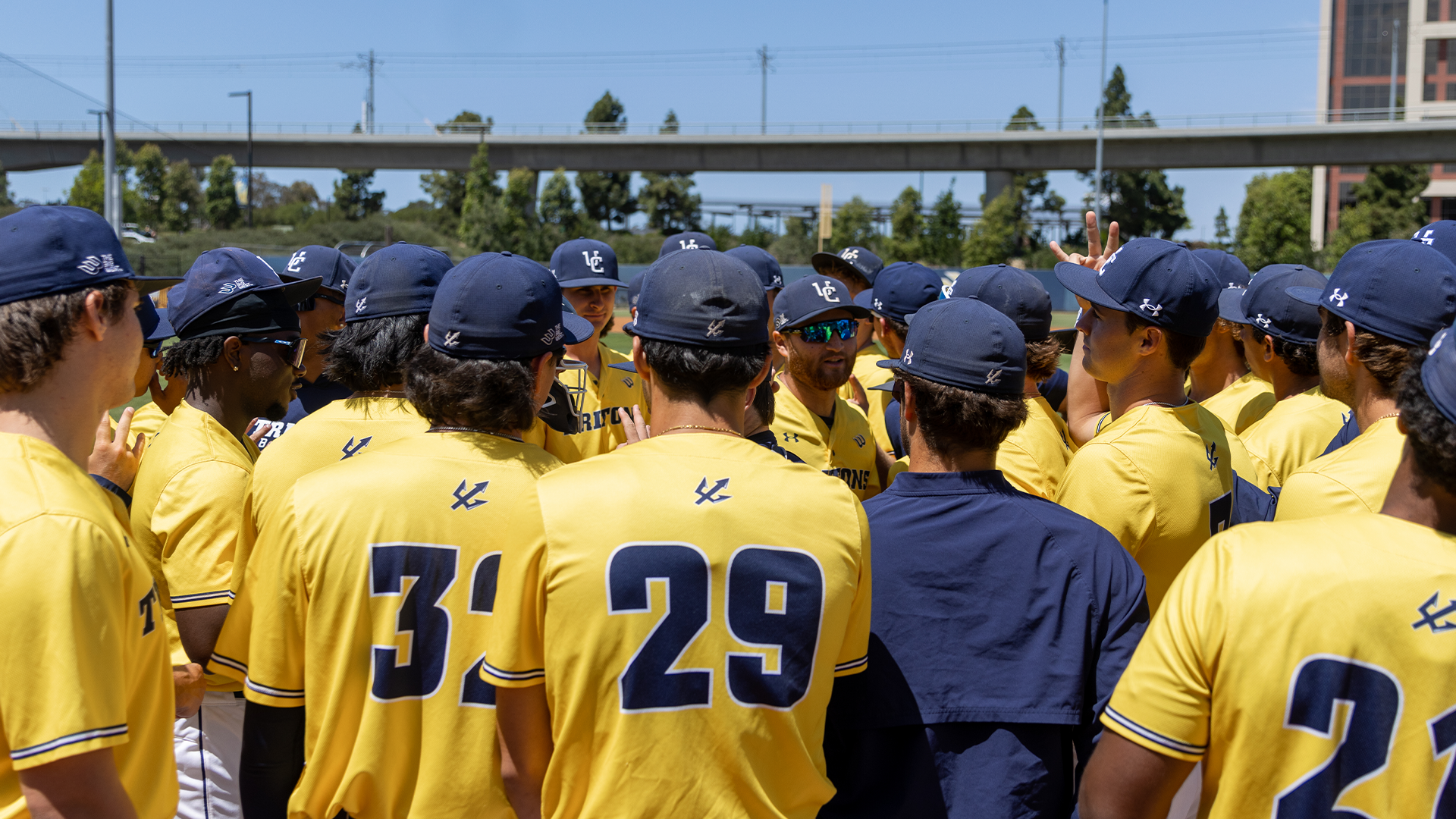 Baseball team huddles in yellow jerseys with blue hats