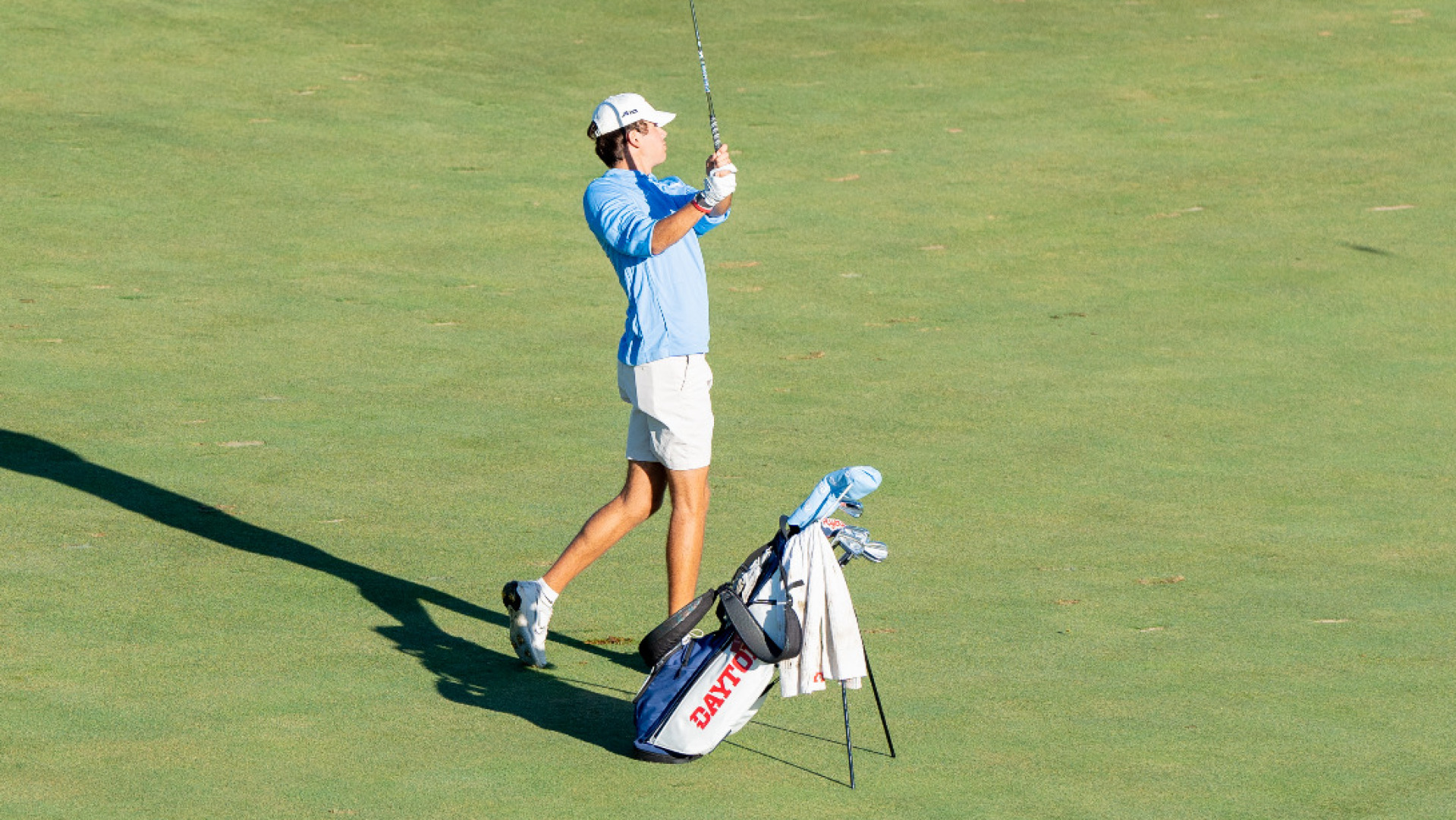Men's golfer J.J. Momper wearing a light blue long-sleeve top and white shirt in his backswing in the fairway at Moraine Country Club with his golf bag to his right