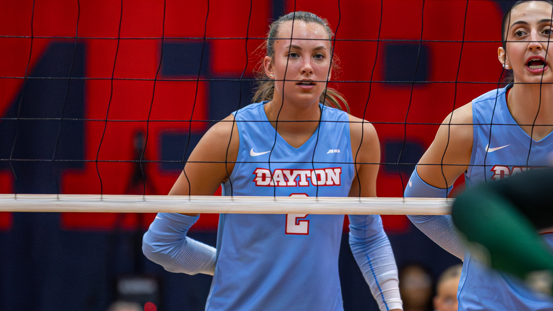Kamryn Hunt stands ready at the net before a serve. Her right arm is behind her back. The net is in front of her.