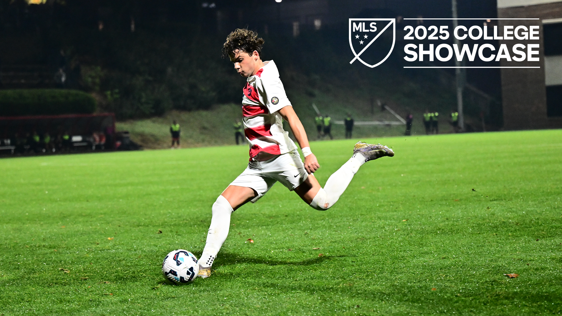 Men's soccer defender Dren Dobruna, wearing a red and white striped jersey with white shorts, prepares to take a shot during a match at Baujan field. White MLS College Showcase logo in the top right corner