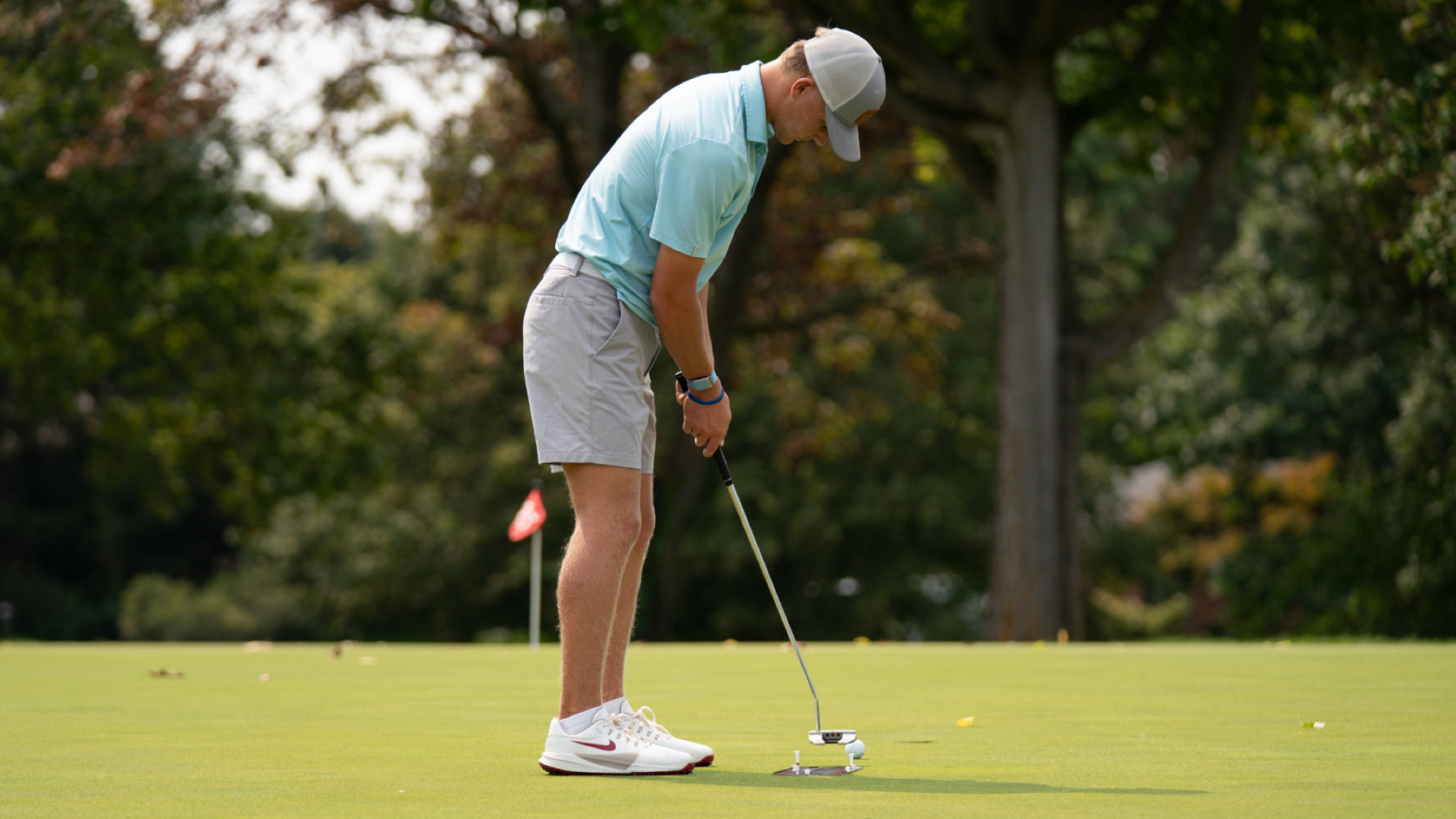 Men's golfer T.J. Kreusch, wearing a light teal polo-style shirt and khaki-colored shots, practicing on a putting green