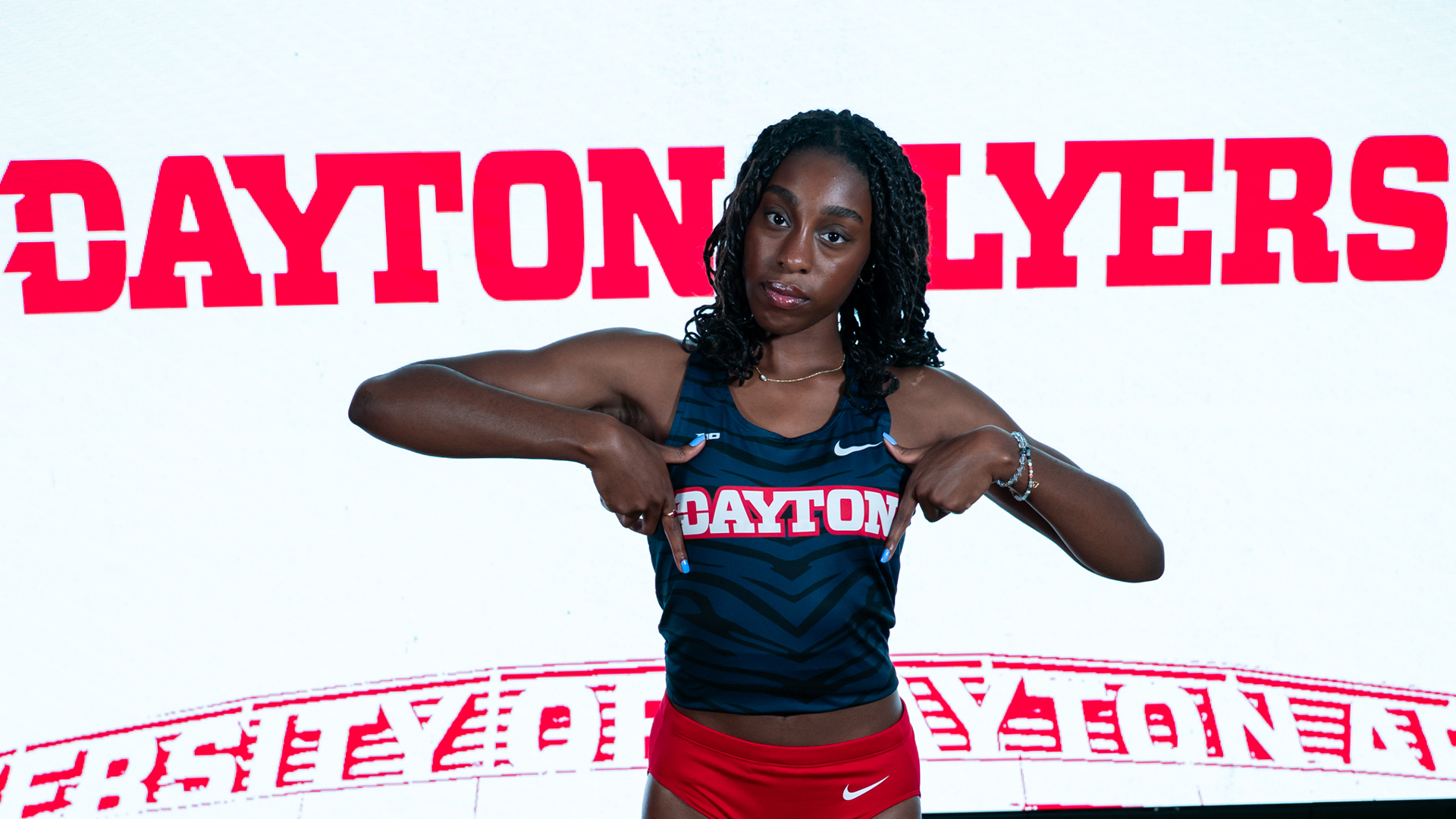 Simone Bessong poses with her hands around her jersey in front of a white background with red 