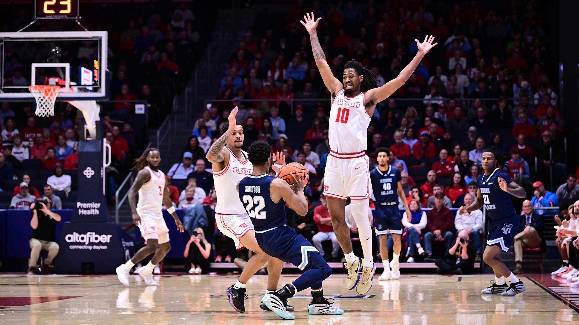 Dayton men's basketball player Bryce Heard jumps in the air playing defense on a Rhode Island player.