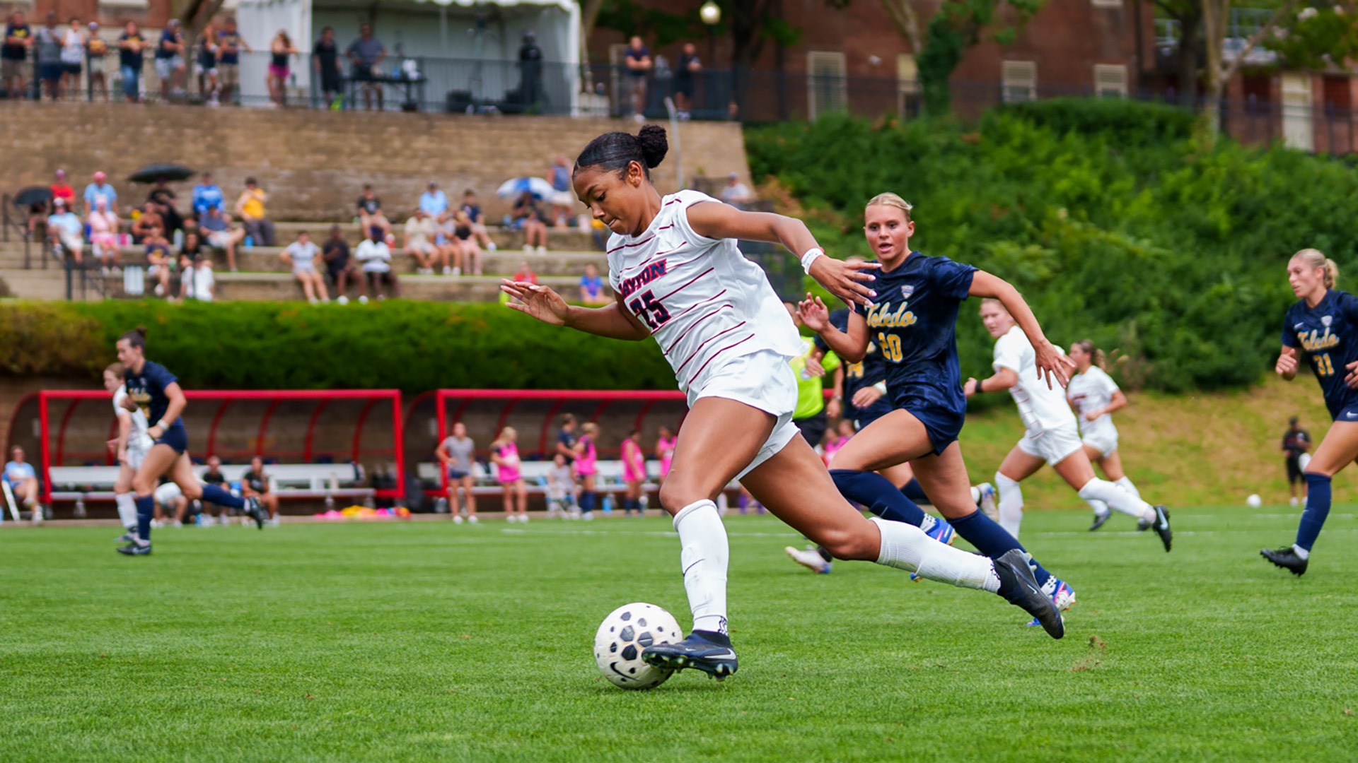 Dayton women's soccer player Ky Hau-Golden, wearing her white jersey with navy Dayton across the chest, dribbles with her left foot against Toledo.