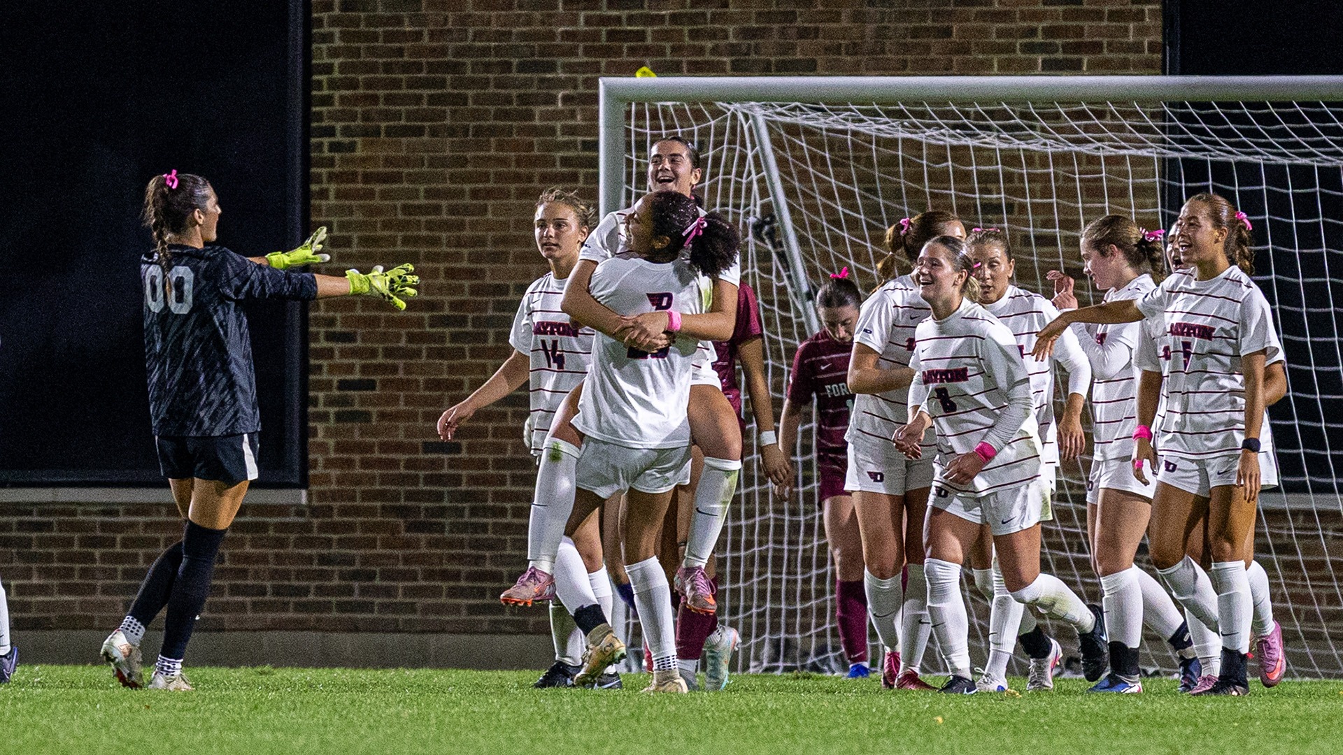 Women soccer celebrate goal hugging in huddle in white jerseys