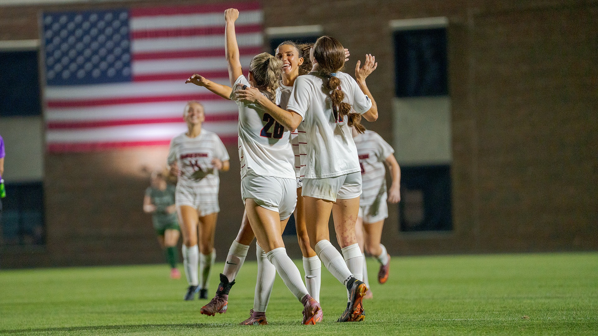 A trio of Dayton women's soccer players celebrate scoring a goal.