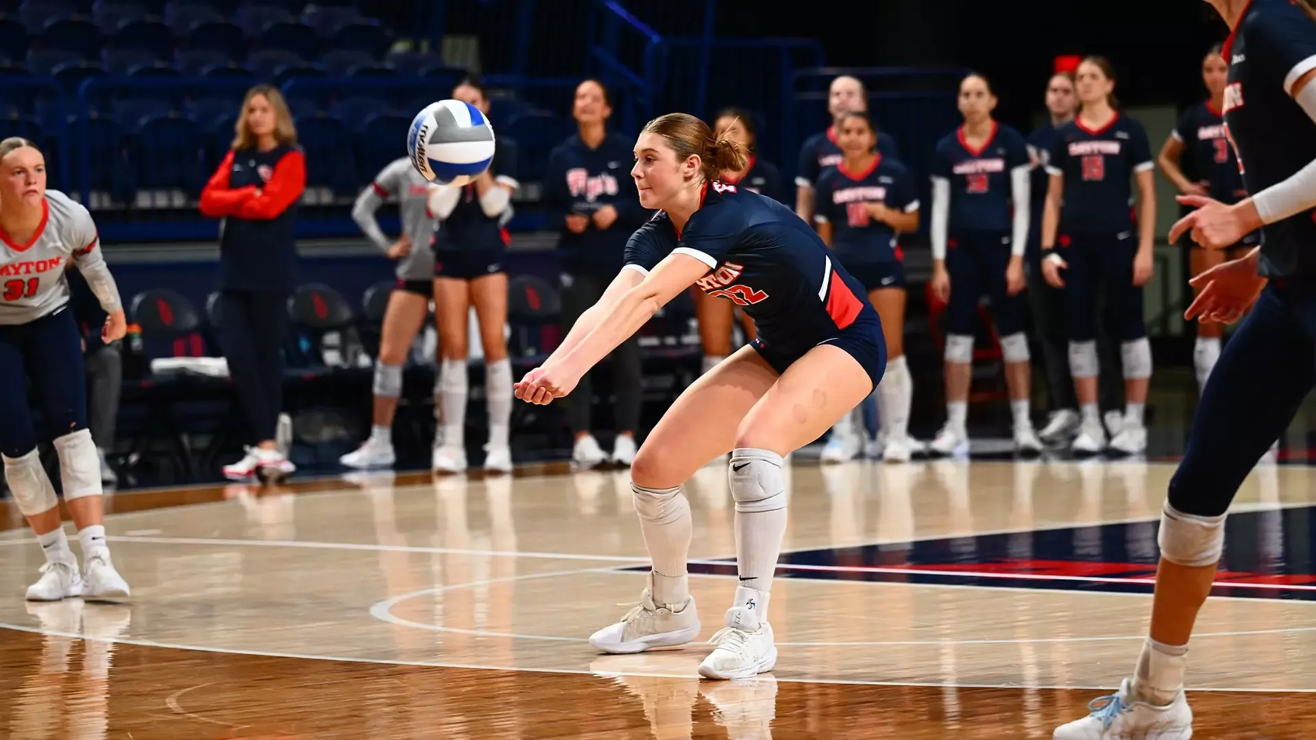 Sidney Sprada digs the ball. She is wearing an all navy uniform.