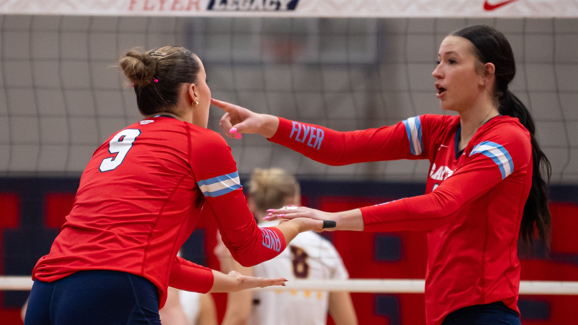 Charlotte Vinson and Natalie Harrington high-five and strategize before the serve. They are wearing red jerseys.
