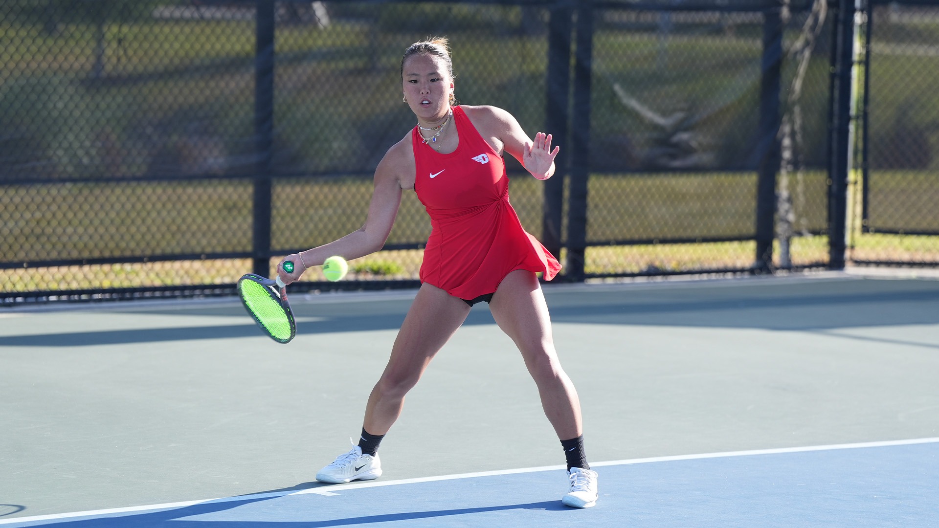 Christian Chin winds her racquet back to hit the ball. She is in a red dress.