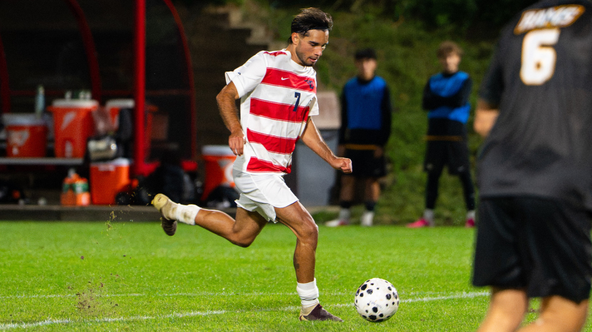 Men's soccer player Pablo Martinez, wearing a red and white striped jersey with the number seven with white shorts and socks, dribbles the ball down field during a match at Baujan Field