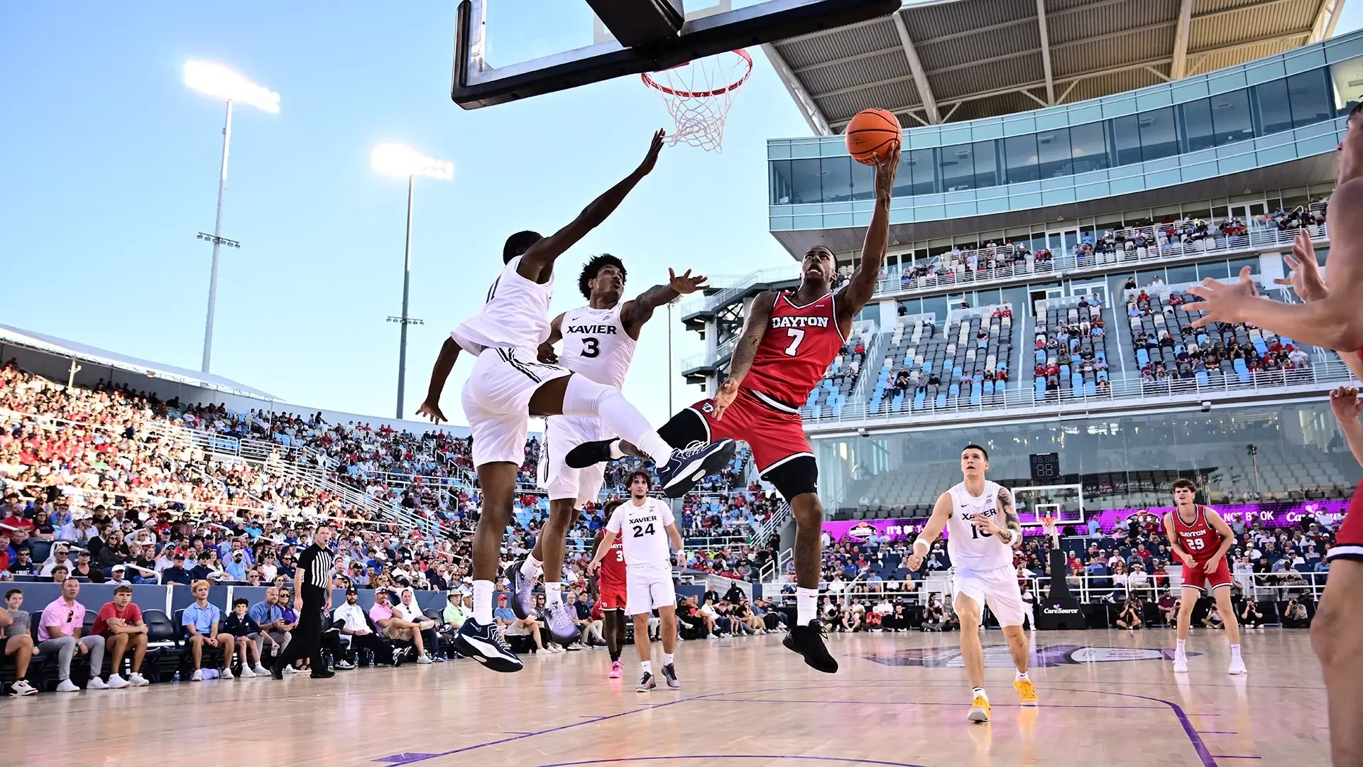 Zaide Lowery goes up for a layup on the right as two Xavier players go up on the left in defense. He is wearing a red uniform, while the Xavier players are in white.