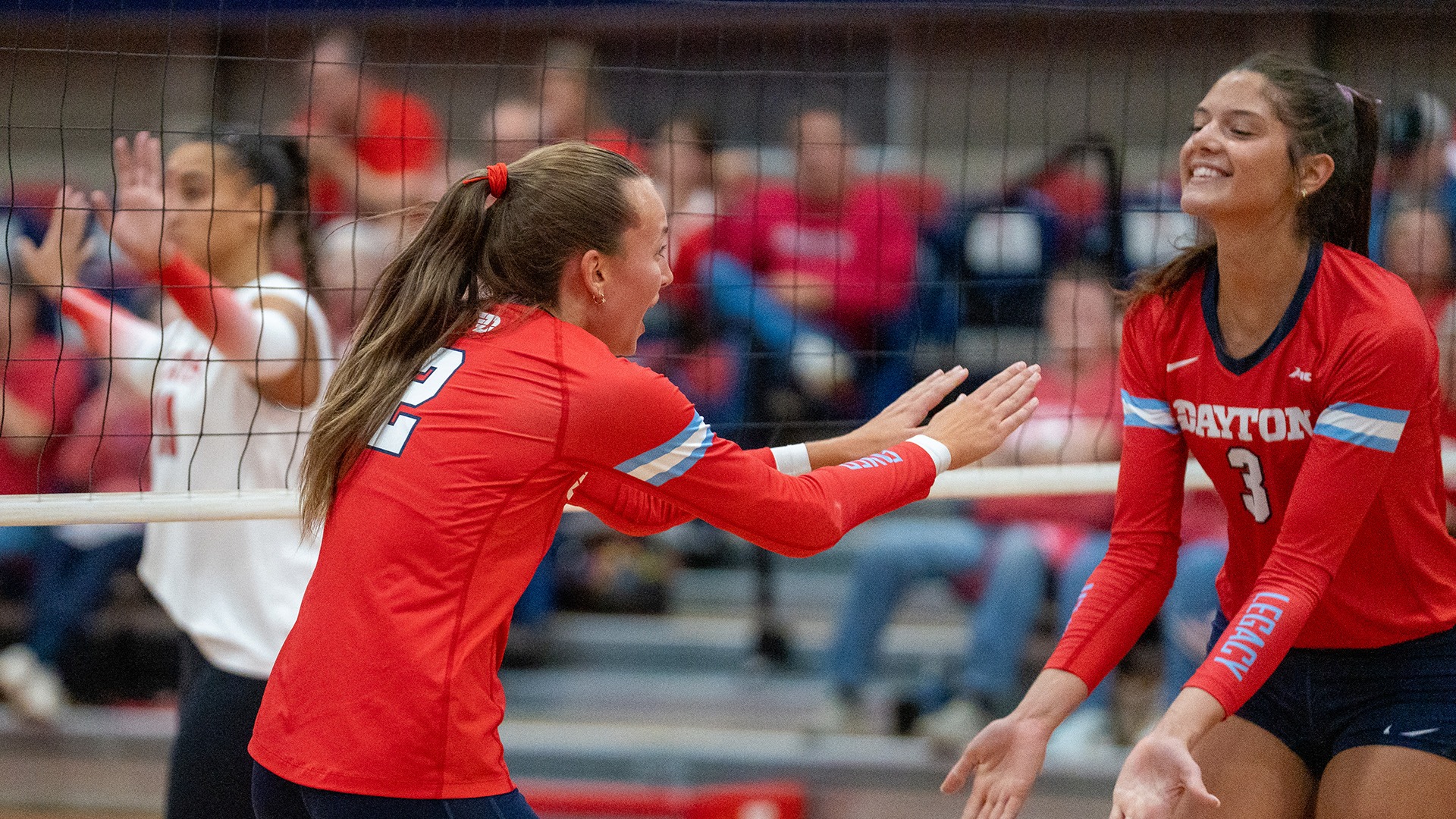 Kamryn Hunt and Abigail Cresse high five with both hands after a point. They are wearing red jerseys and a navy pants.