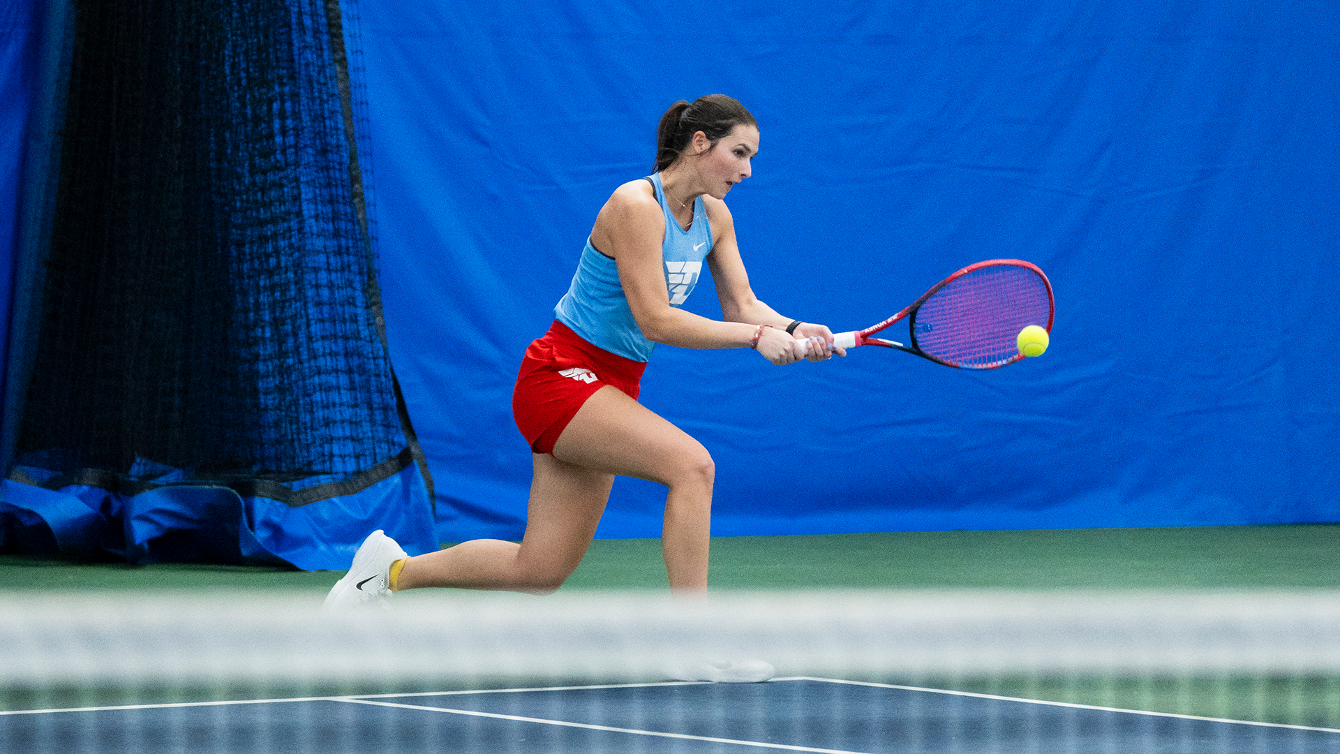 Grace Murphy lunges to hit the ball. Her racquet is in both of her hands.