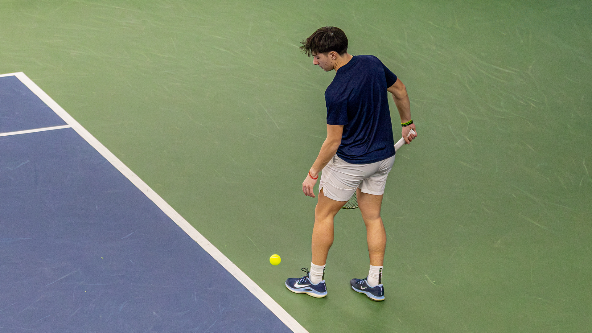 Kyle McNally bounces a ball on the ground before a serve. His back is to the camera.