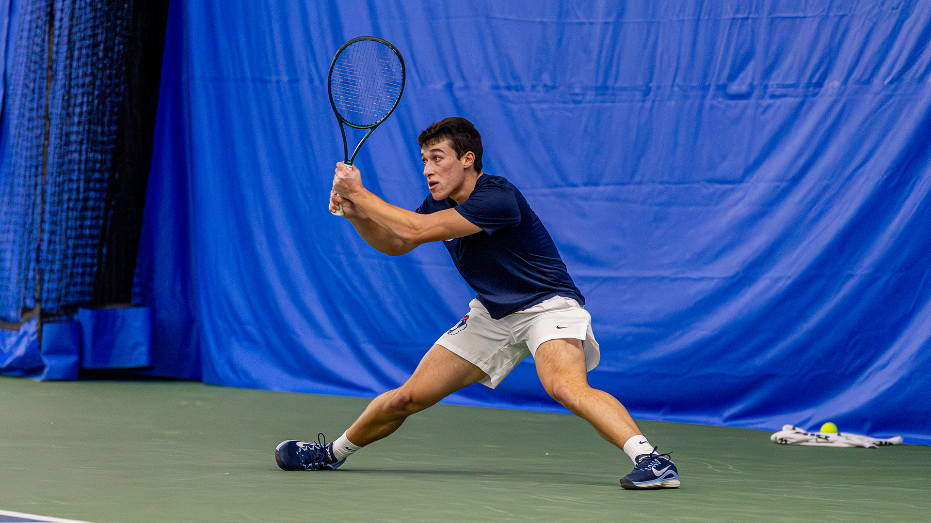 Mikkel Zinder stands nearly in a split with his racquet up in front of him.