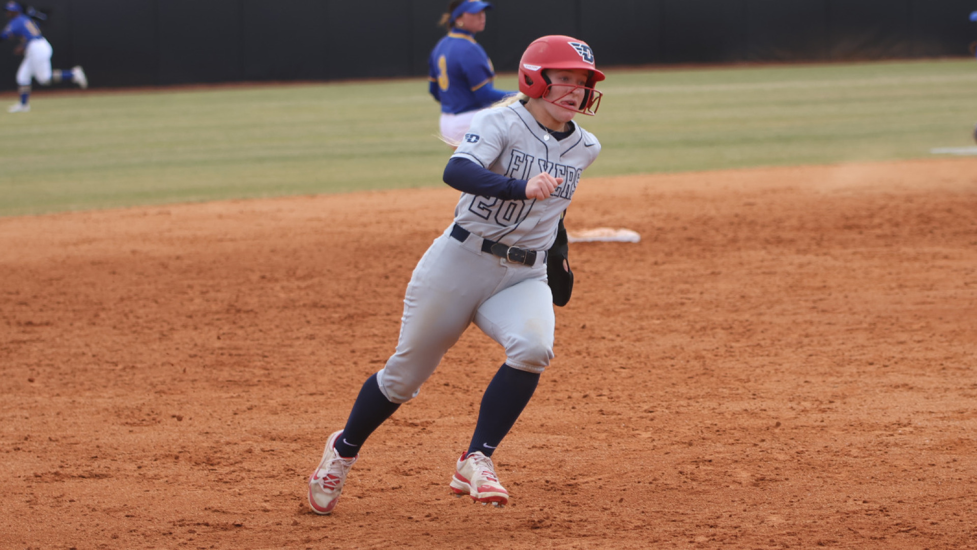 Softball's Maura Carmody, wearing a gray and blue uniform and red batting helmet, running the base path from second to third during a game against Morehead State