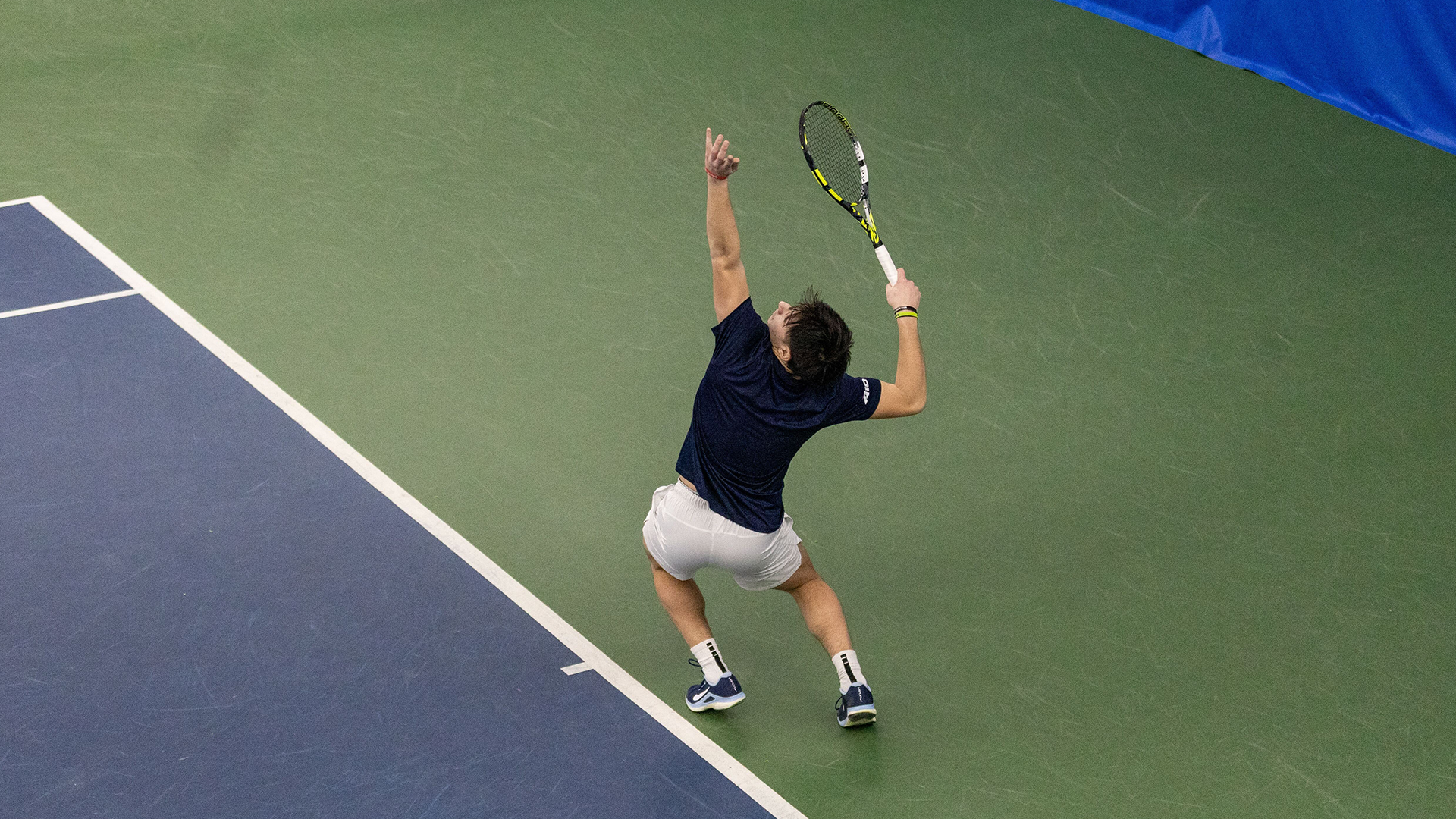 Kyle McNally serves the ball. His back is to the camera and the ball is out of frame.