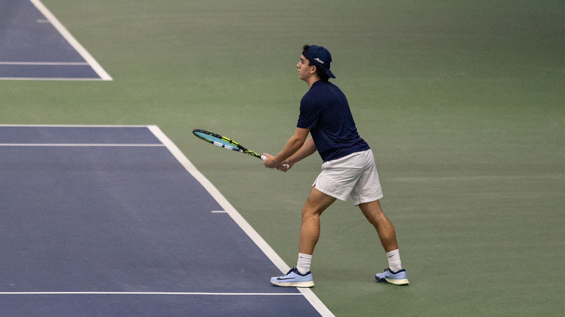 Dylan Jaen stands ready for the serve with his left foot forward and his racquet in both hands.