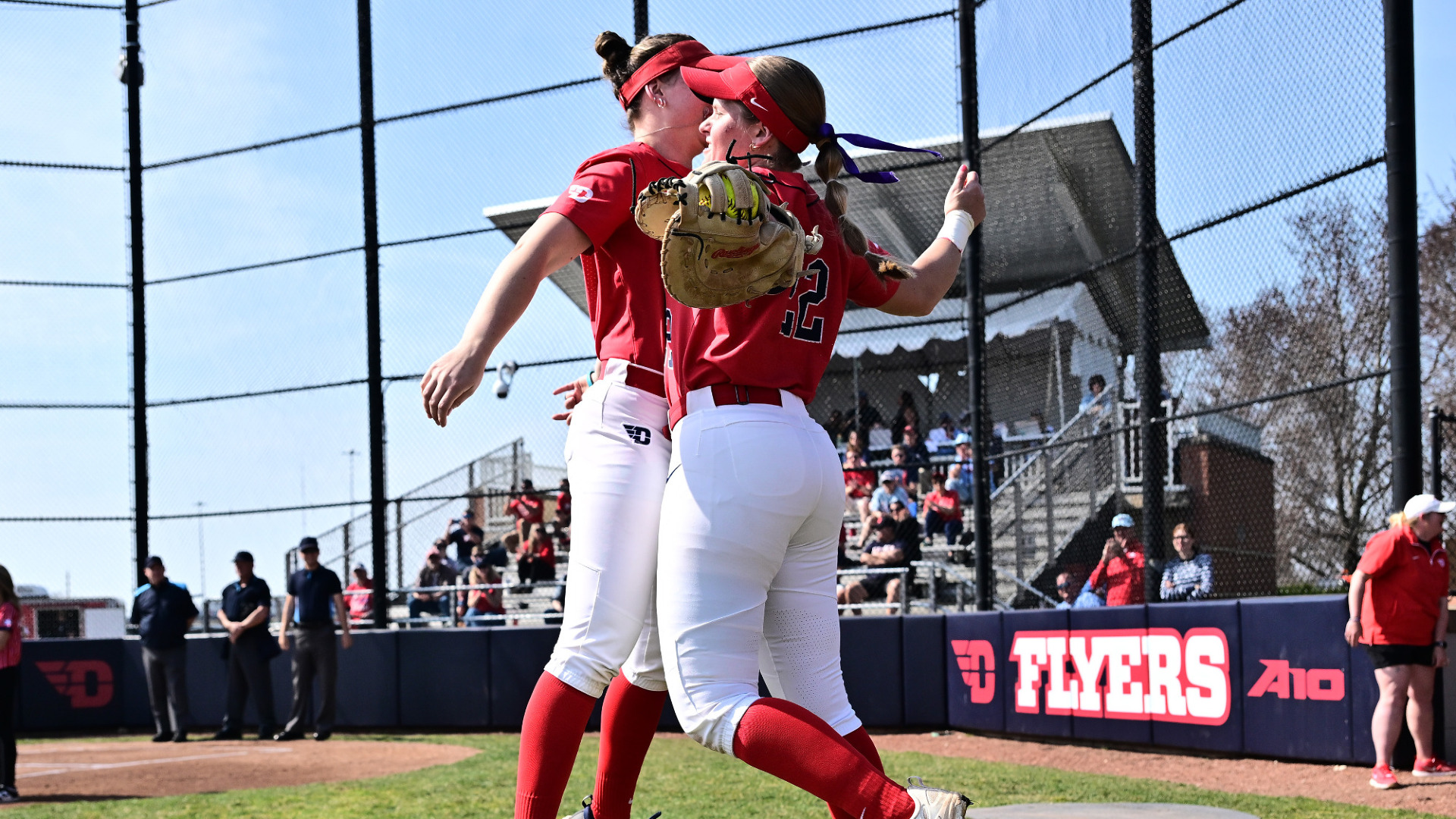 Softball players Izzy Kemp and Molly Grace, wearing red jerseys and white uniform pants, chest bump during starting lineups ahead of a game at UD Softball Stadium