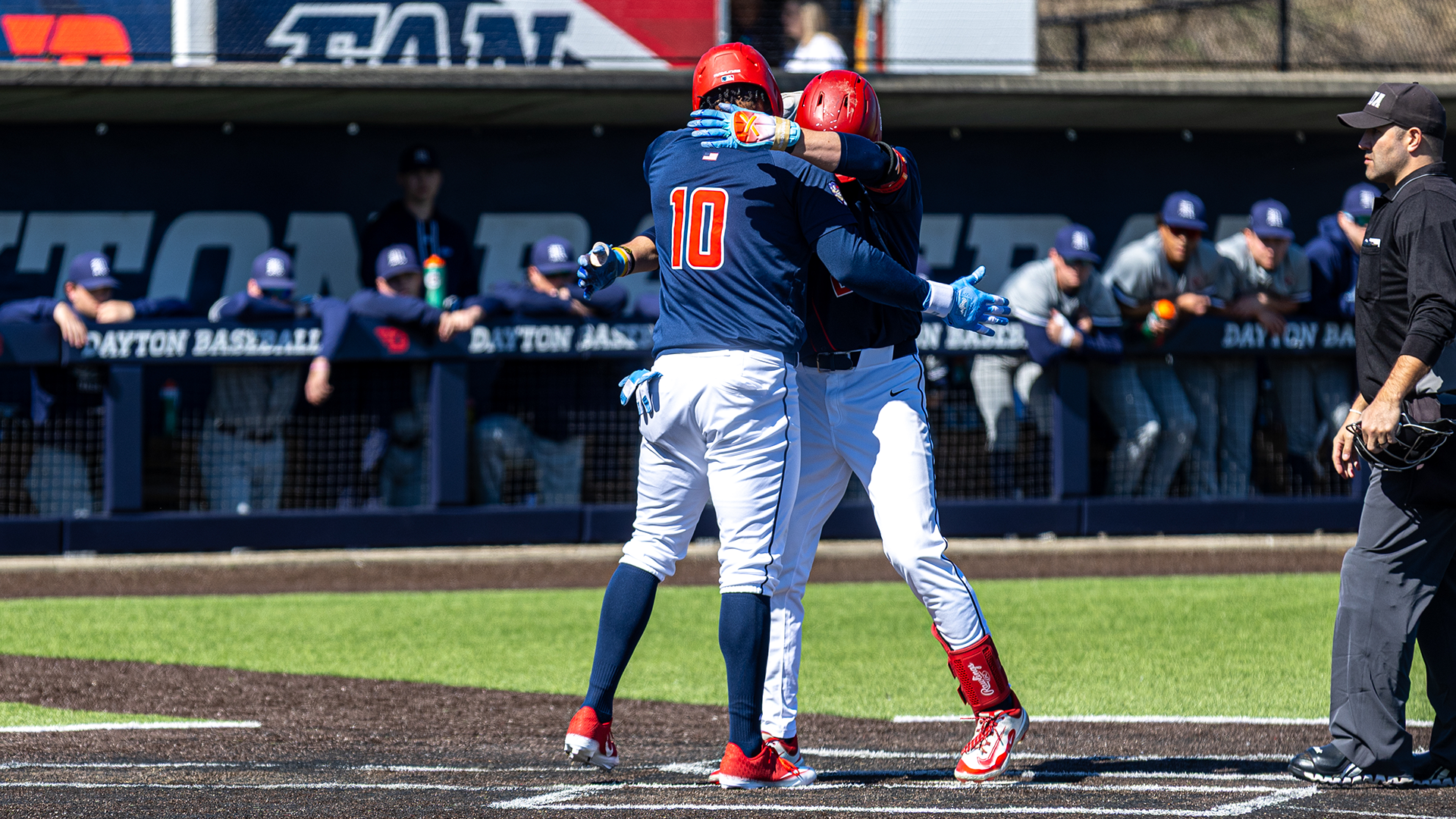 Michael Smith Jr. embraces a teammate at home plate. They are wearing navy jerseys and white pants.