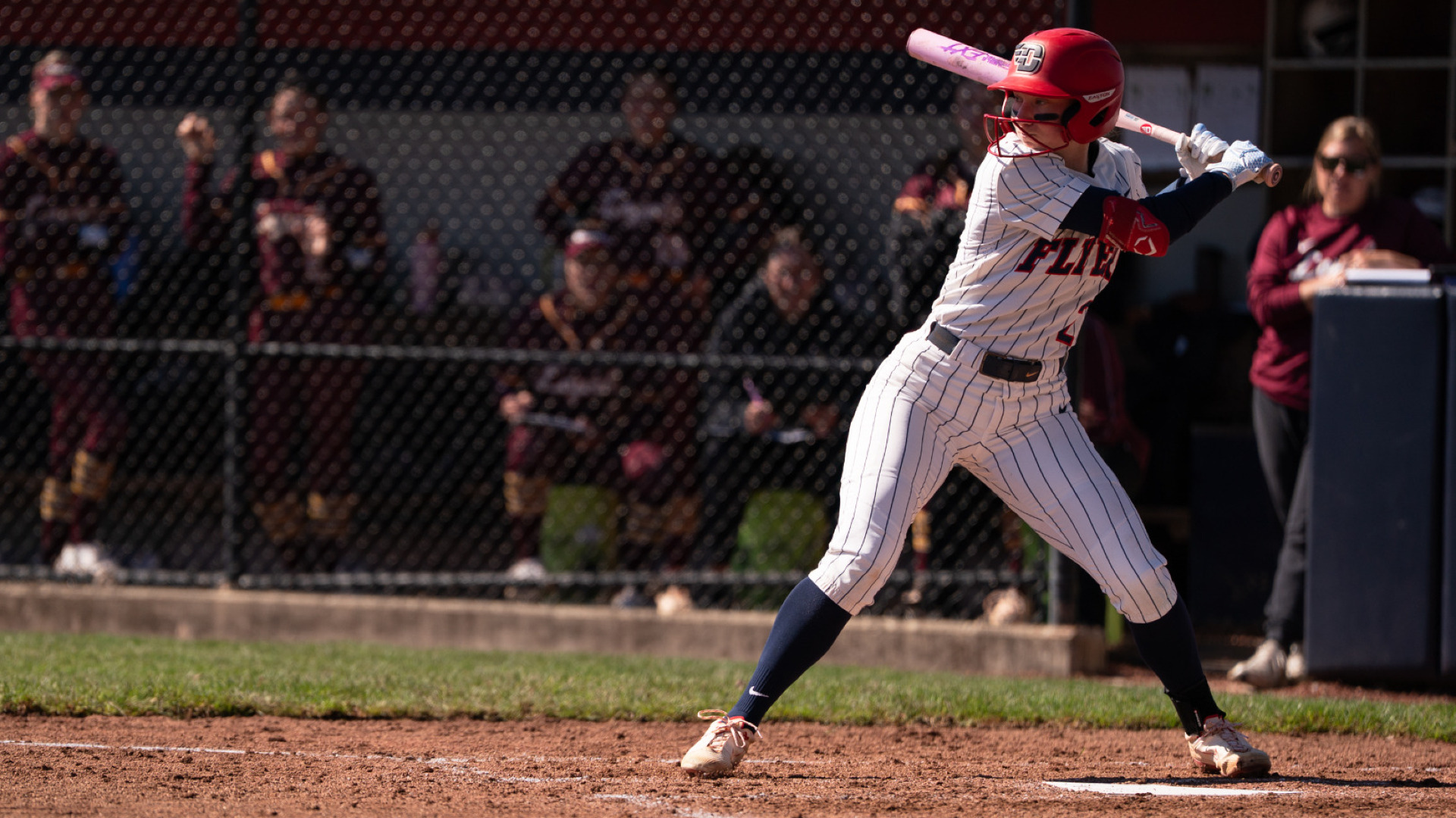 Softball's No. 2 Kirnan Bailey, wearing a white pin stripe uniform and red batting helmet, stands in the batter's box with her bat on her shoulder awaiting a pitch in a game at UD Softball Stadium