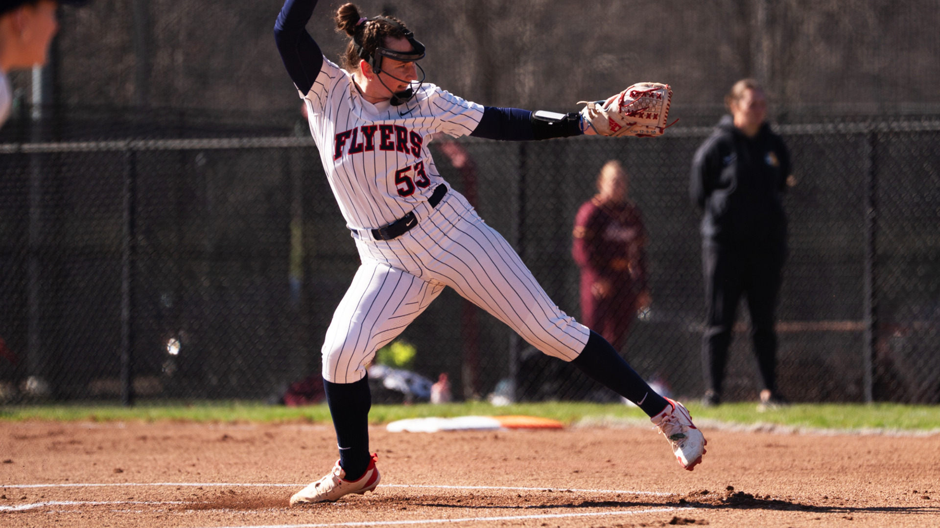 Pitcher Izzy Kemp, wearing a white pinstripe uniform with the number 53, with the ball above her head in the top of her pitching motion during a game at UD Softball Stadium