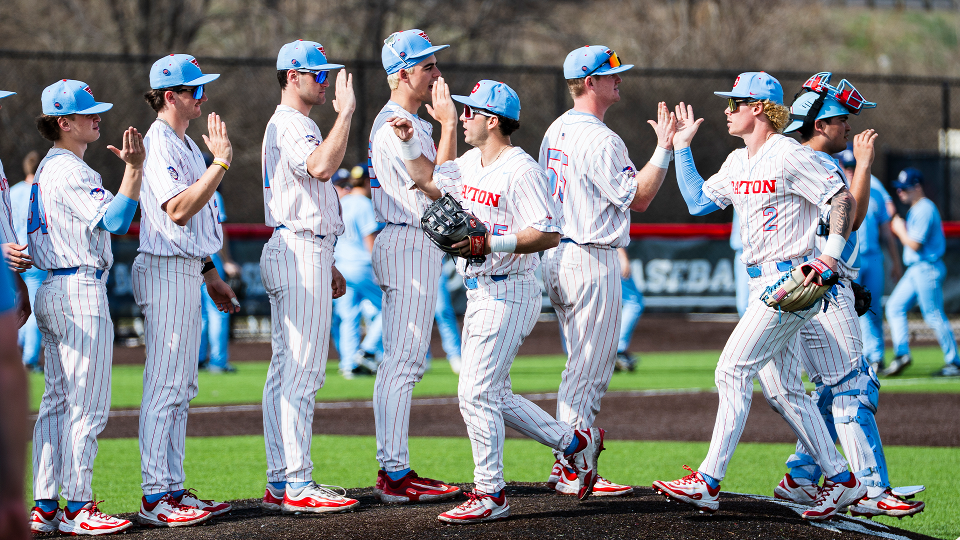 Players in white pinstripe uniforms high five each other after a game.