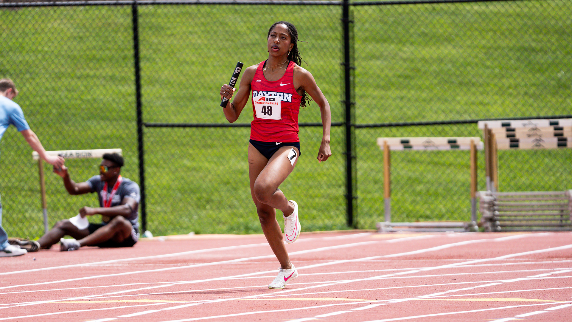 Mariya Washington runs around the bend with a baton in her hand at A-10 Outdoors