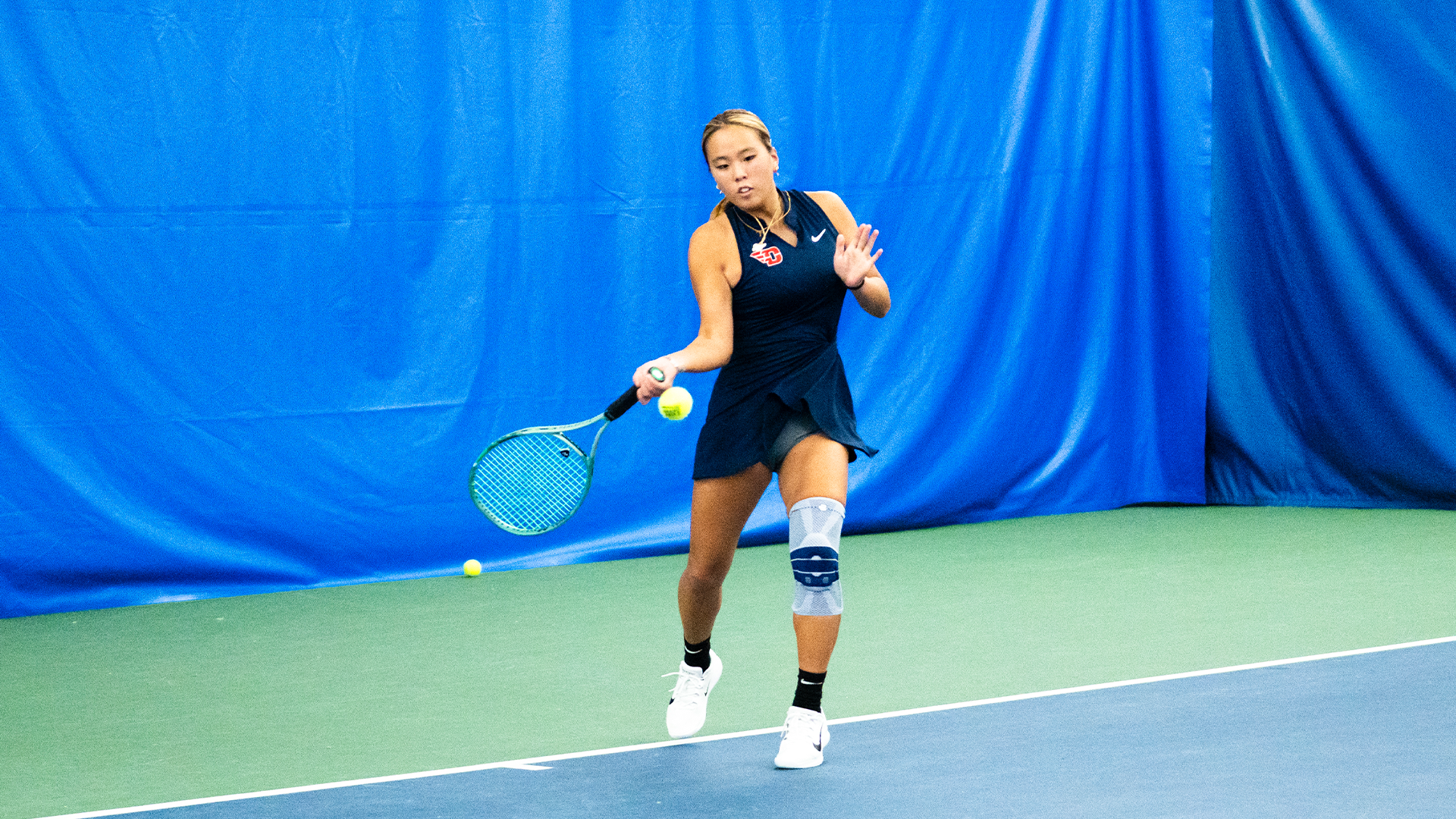 Christian Chin swings her racquet down low to hit the ball in the left side of the frame.