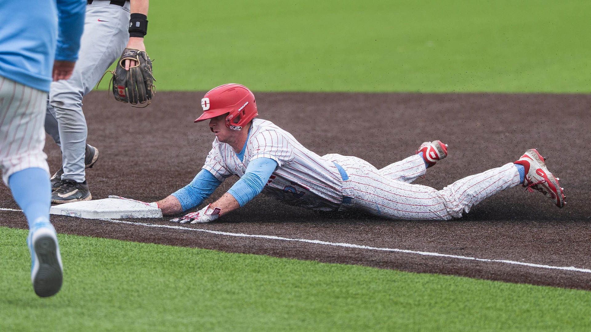 Danny MacDougall lays on the ground and reaches for third base, sliding to steal the base.