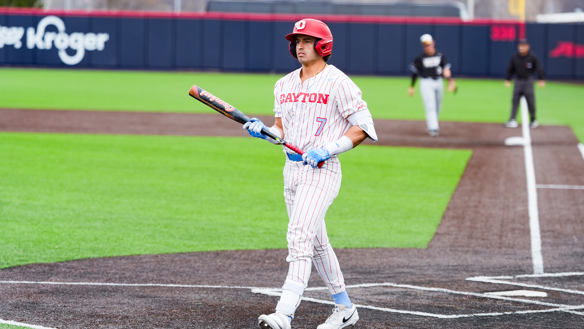 Jason Bello holds his bat in both hands as he walks from the dugout to the right-handed batter's box.