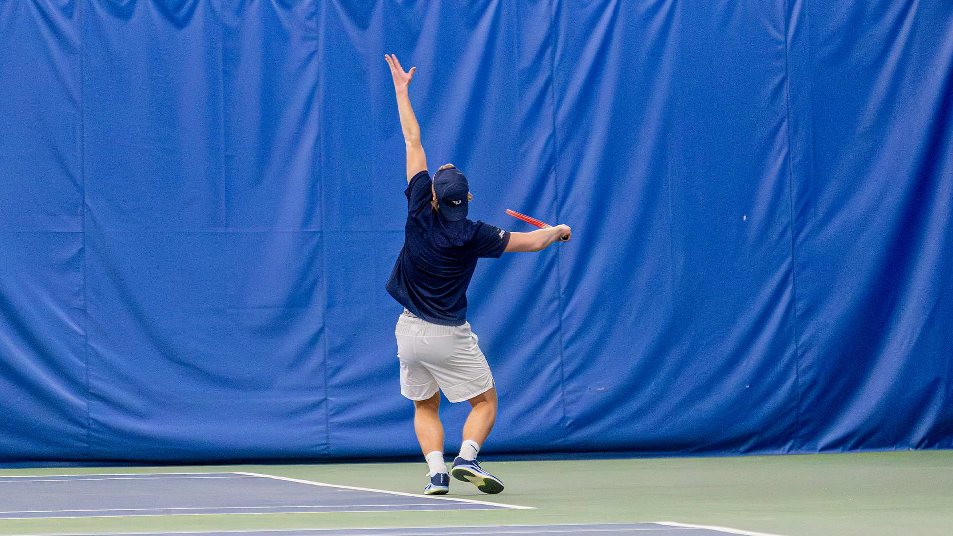 Sturle Skigelstrand throws a ball into the air to serve. His back is to the camera.