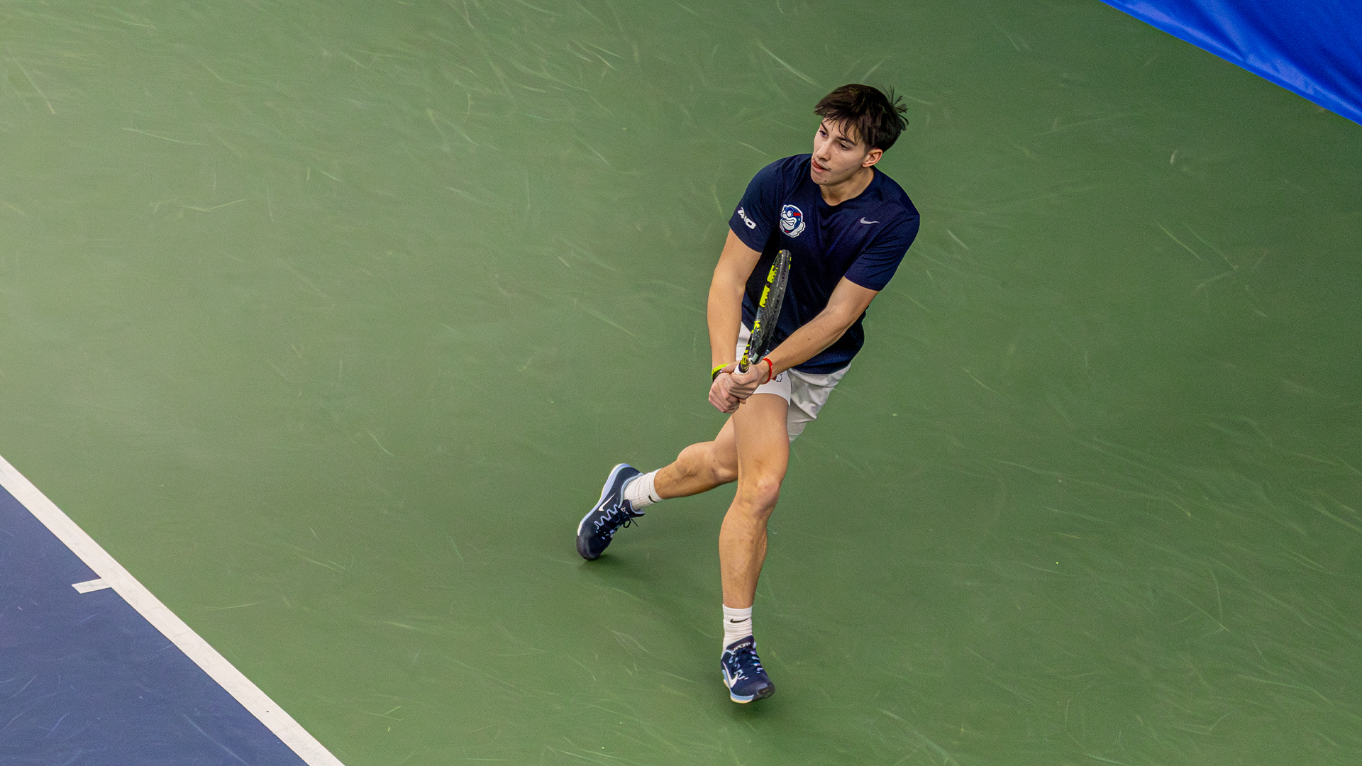 Kyle McNally crosses over himself to return the ball. He's holding his racquet in both hands.