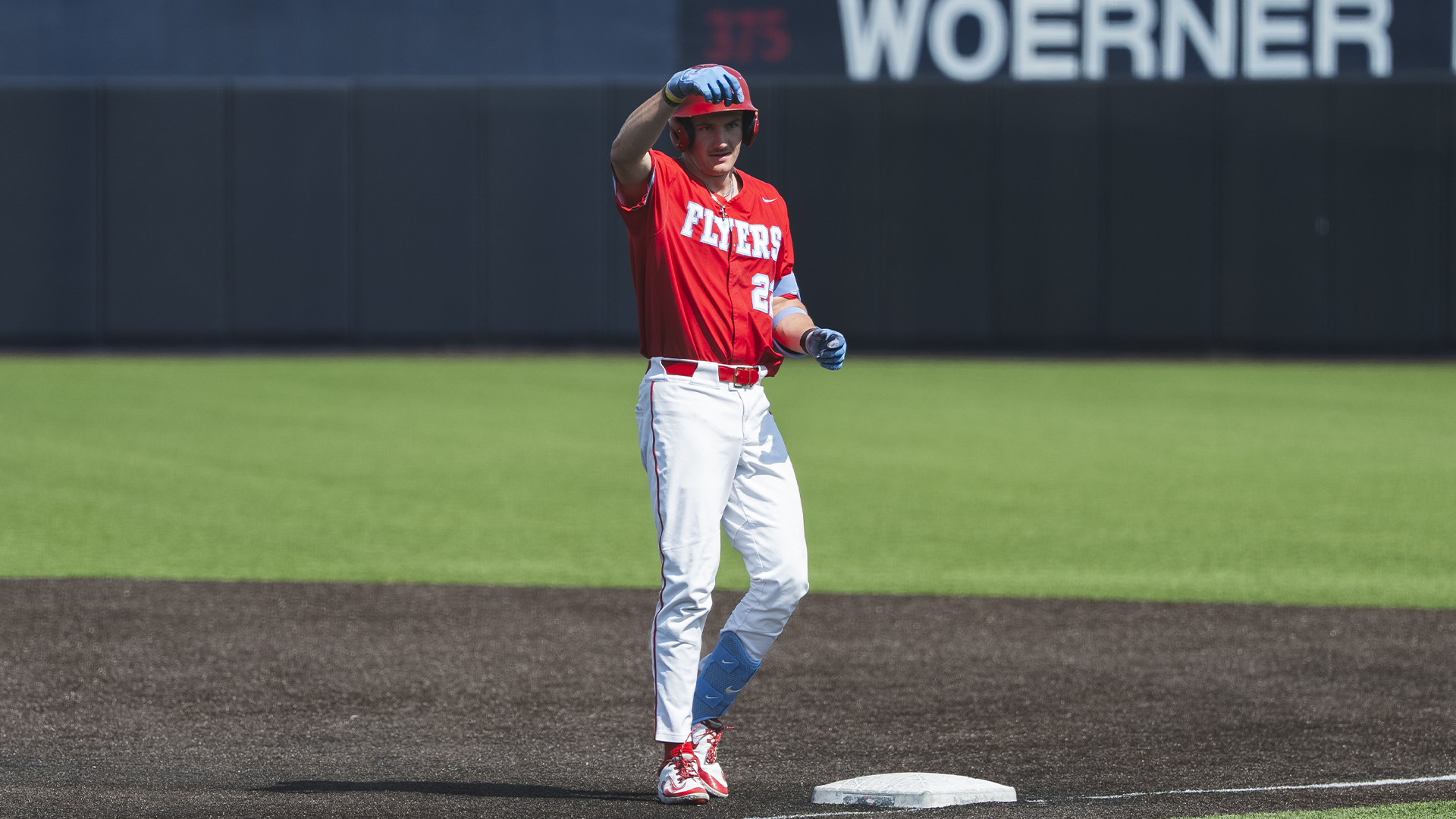 Colin Lynch, standing on first base, turns to celebrate with the dugout after a hit.