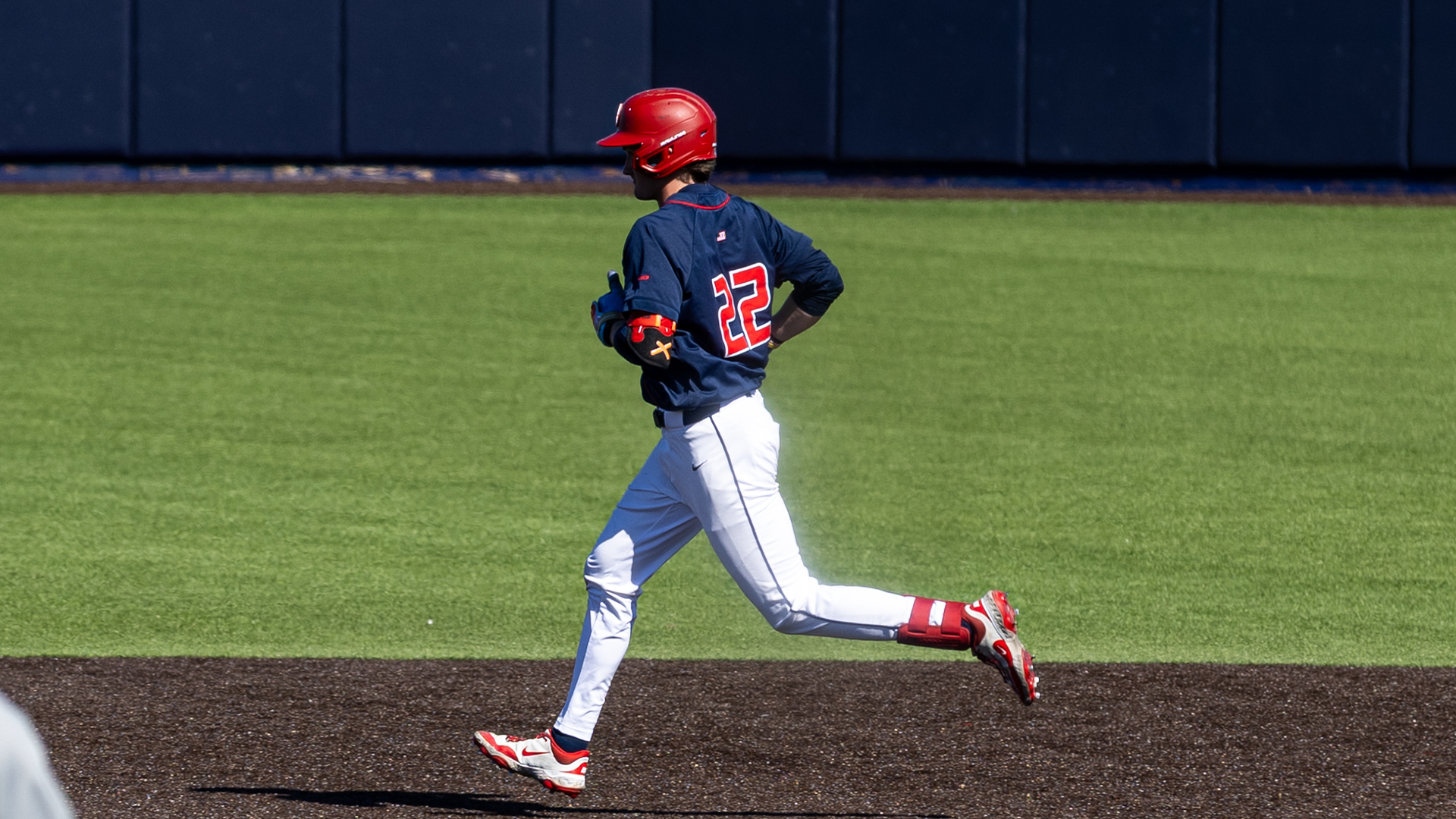 Colin Lynch, wearing a navy uniform shirt, white pants and a red helmet, runs from second to third.