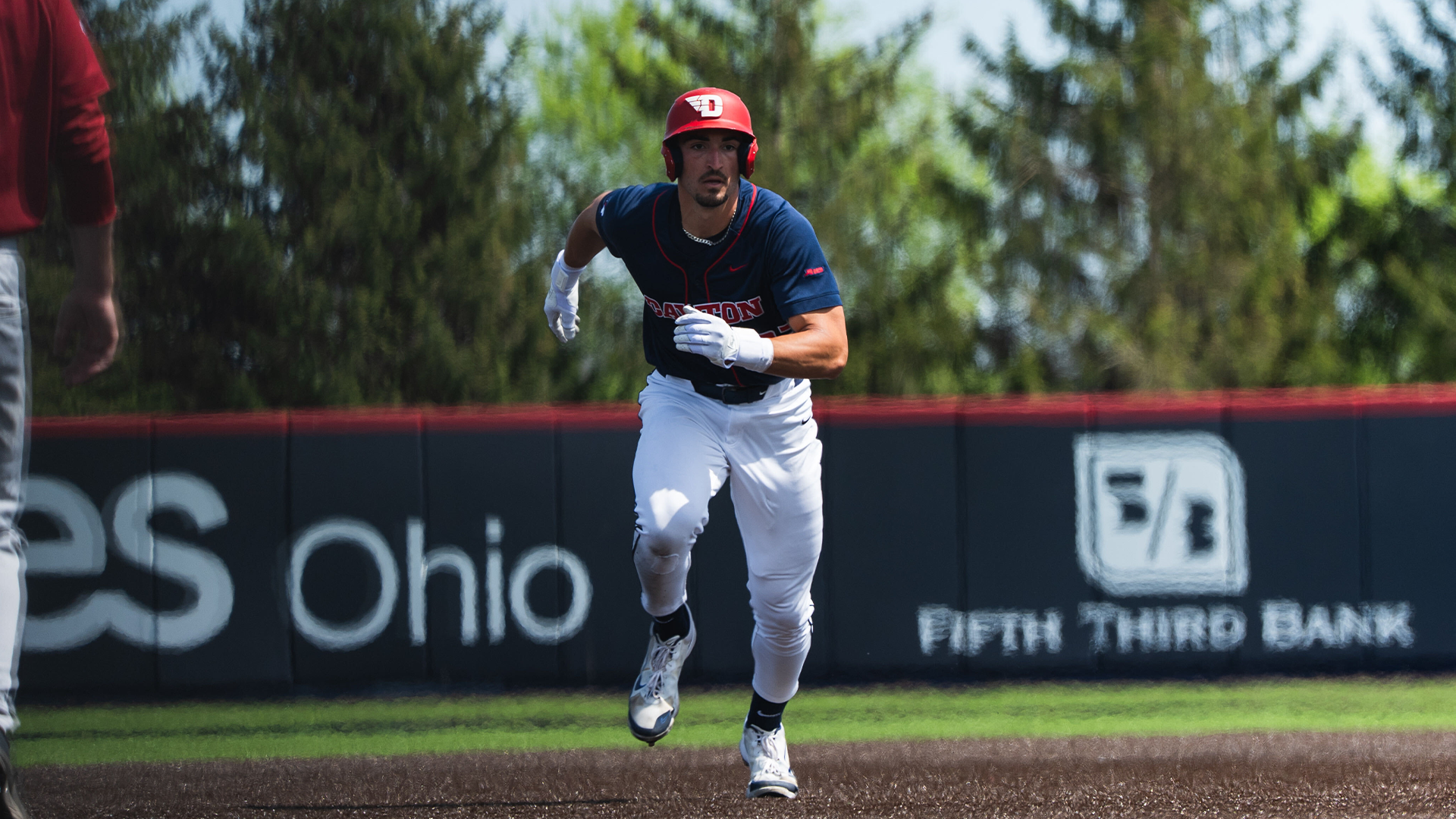 Bobby Stang, wearing white pants, a navy jersey and a red helmet, runs from first to second base.
