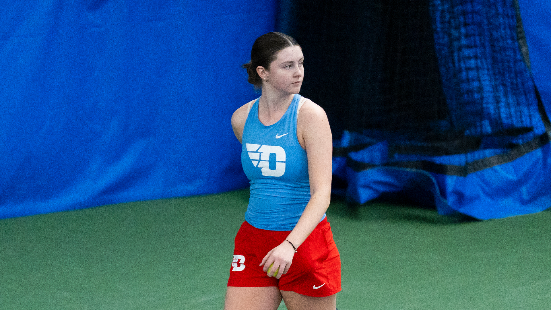 Baby Jordan, wearing a blue tank top and red shorts, walks with he racket behind her.